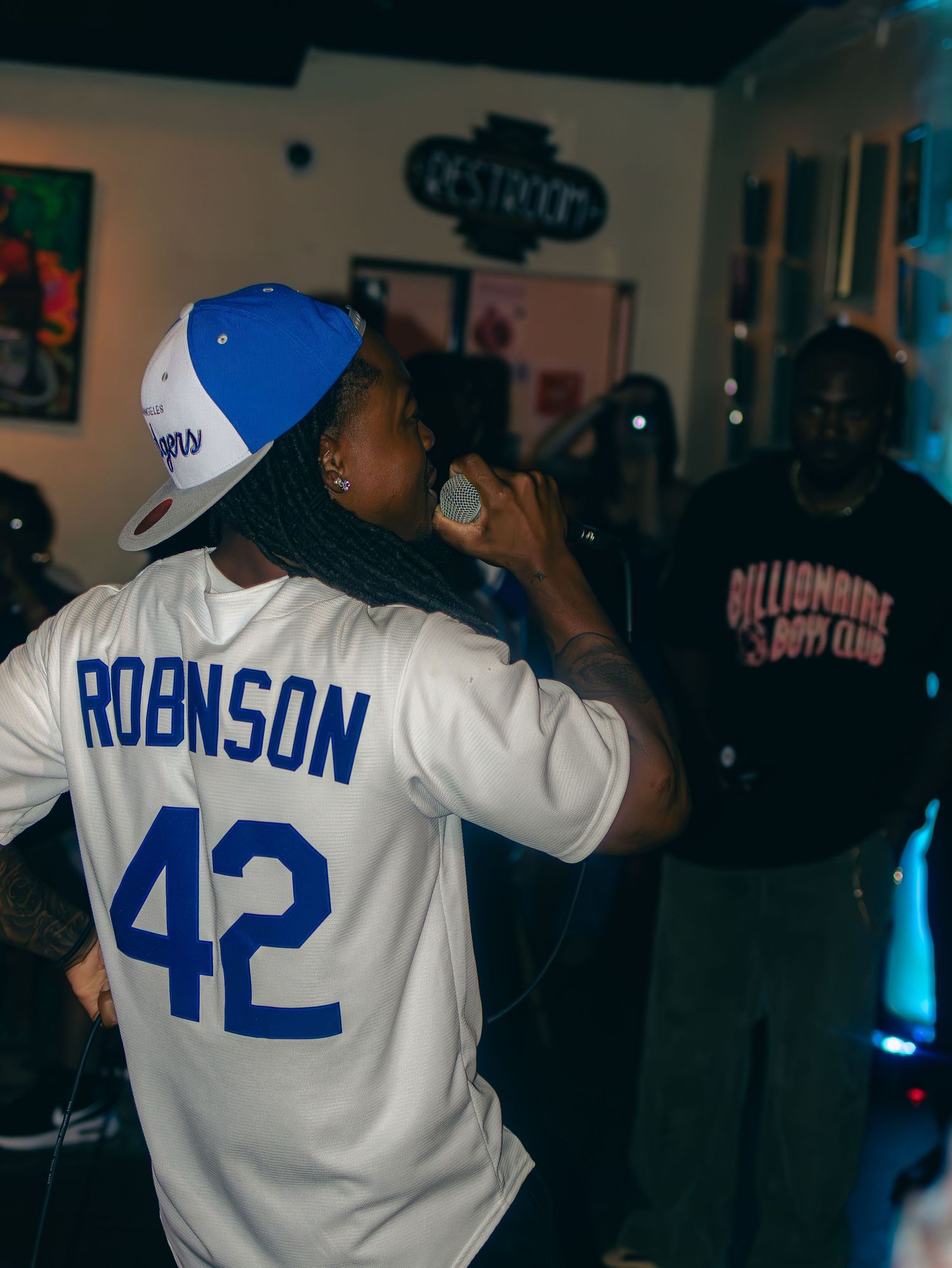 Performer wearing white jersey with number 42 and blue cap performs on stage with colorful lighting.