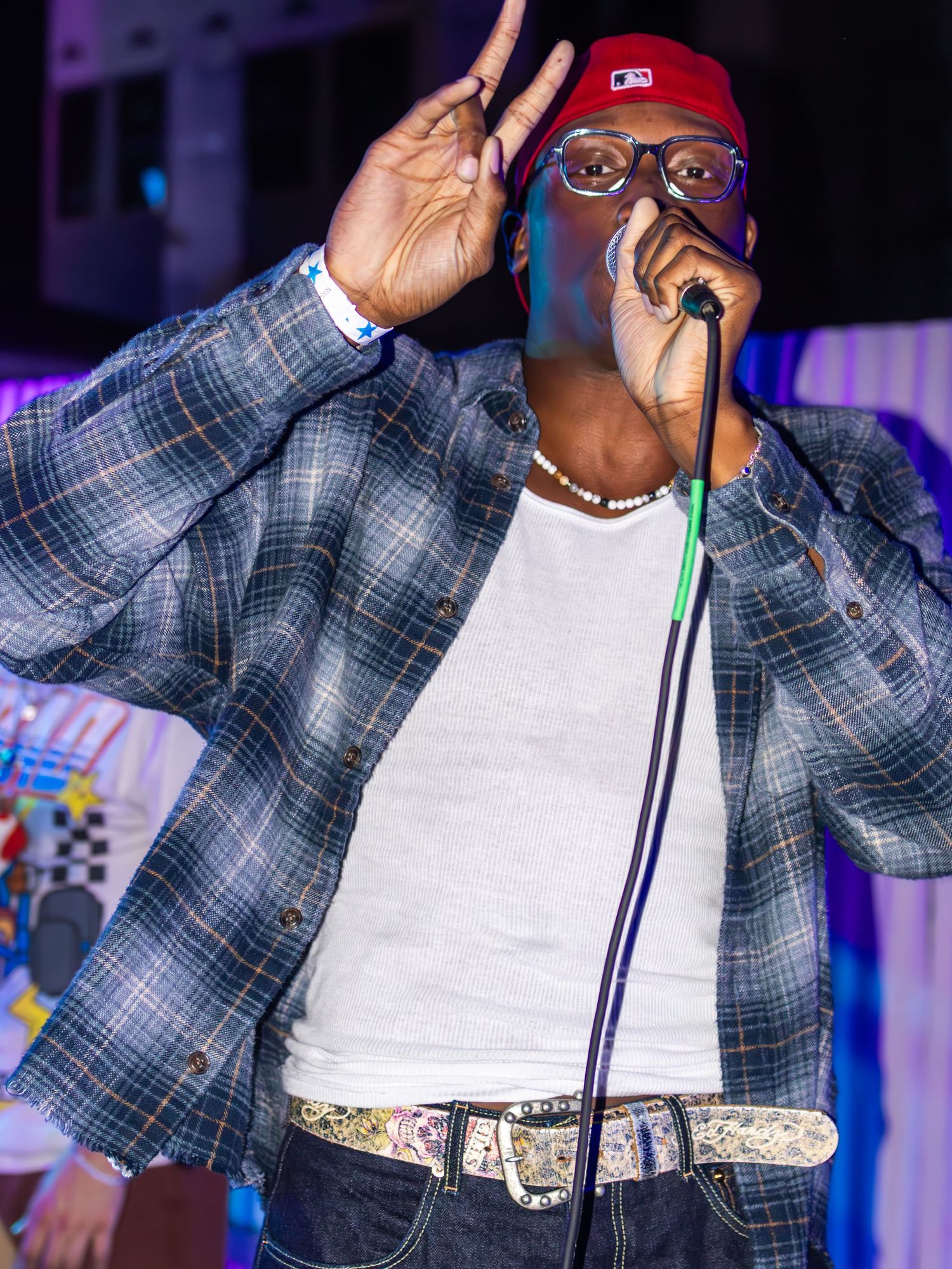 Singer in plaid jacket performing under purple stage lighting at night venue.