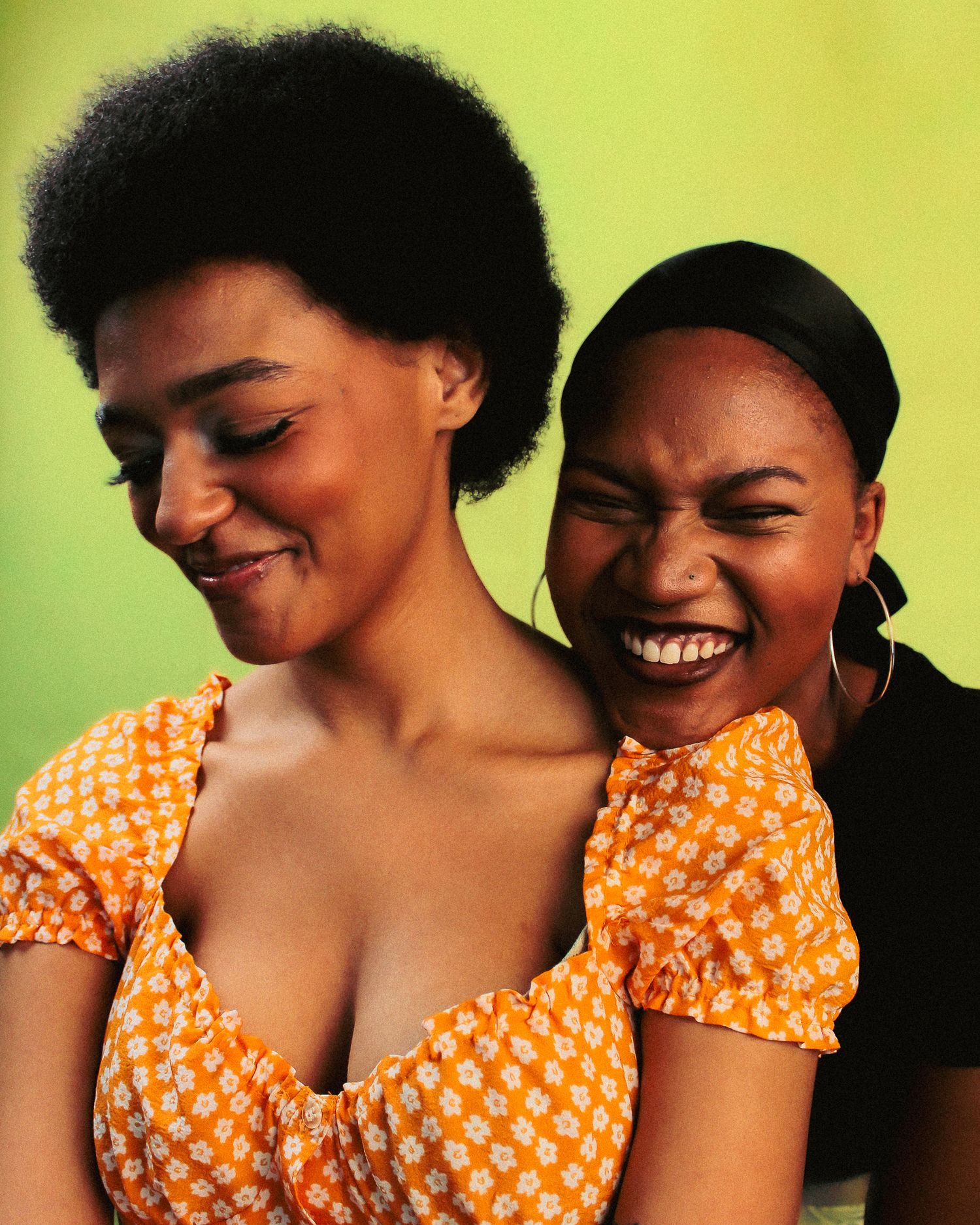 Two people share joyful laughter while wearing orange polka dot clothing against yellow backdrop.