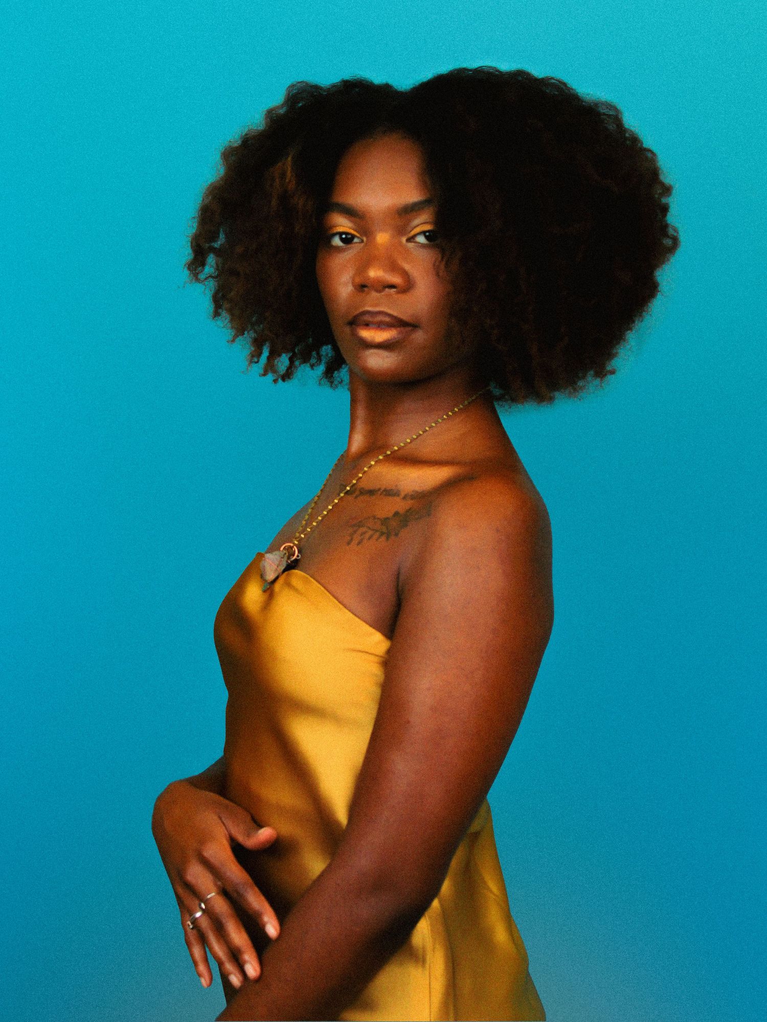 Elegant pose in gold satin top against vivid blue studio background.