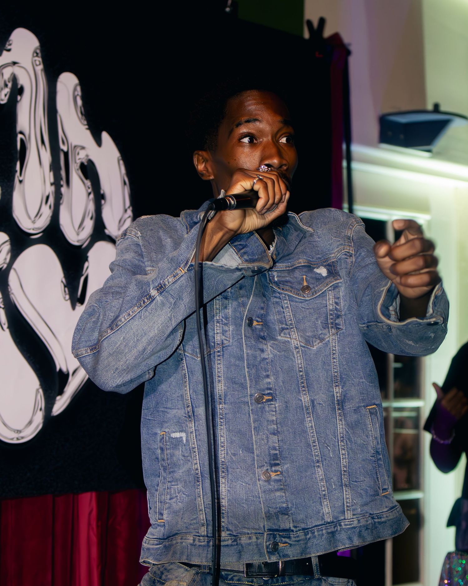 Artist in jean jacket performing with dynamic movement on stage with dramatic lighting effects.