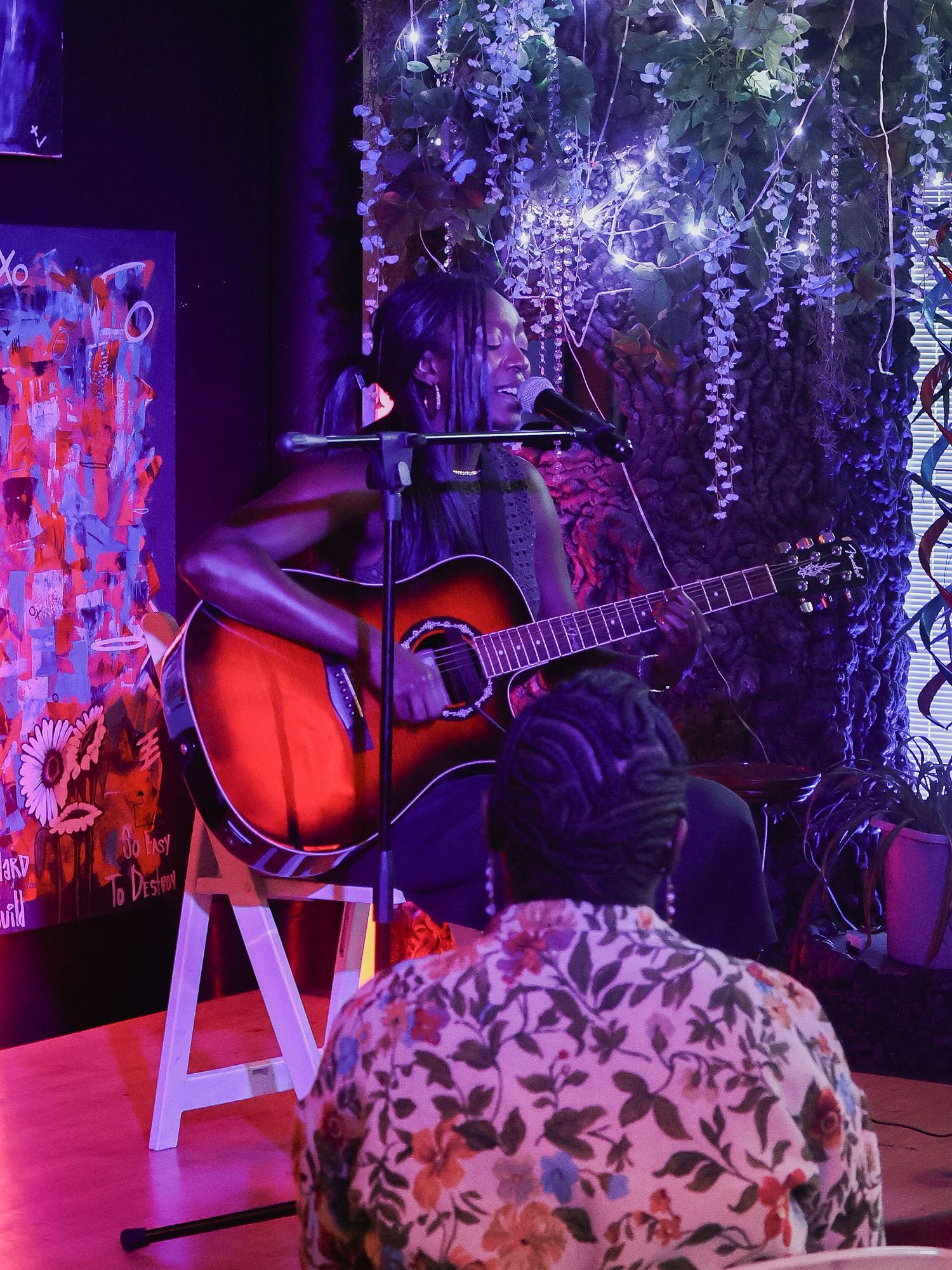 Purple-lit stage setup with acoustic guitar and floral decorations against artistic backdrop.