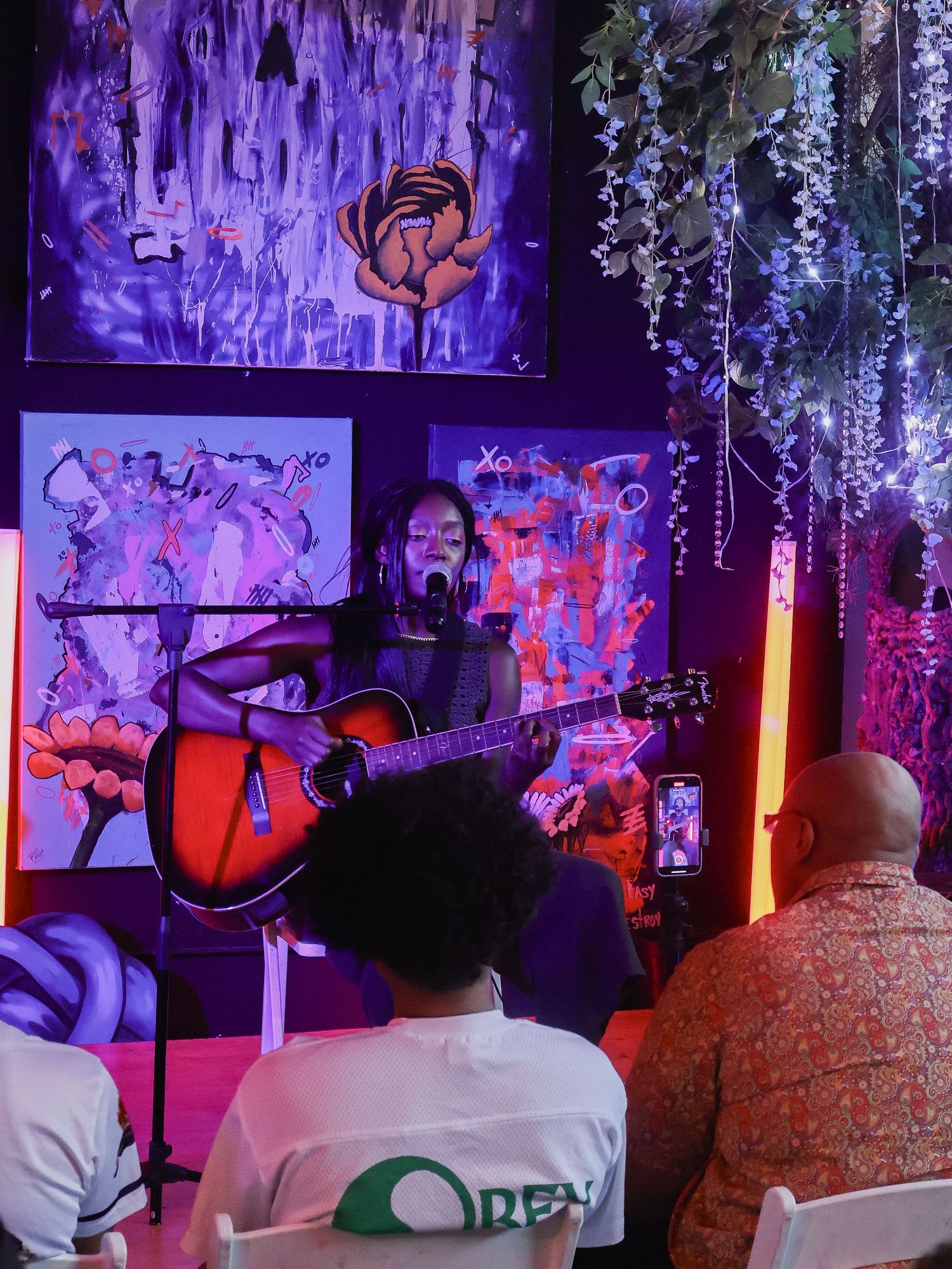 Purple-lit concert venue shows audience members watching performance with decorative lighting elements.