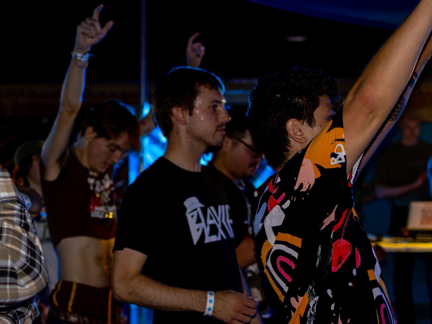 Crowd with raised hands dancing at a nightclub under blue lighting.