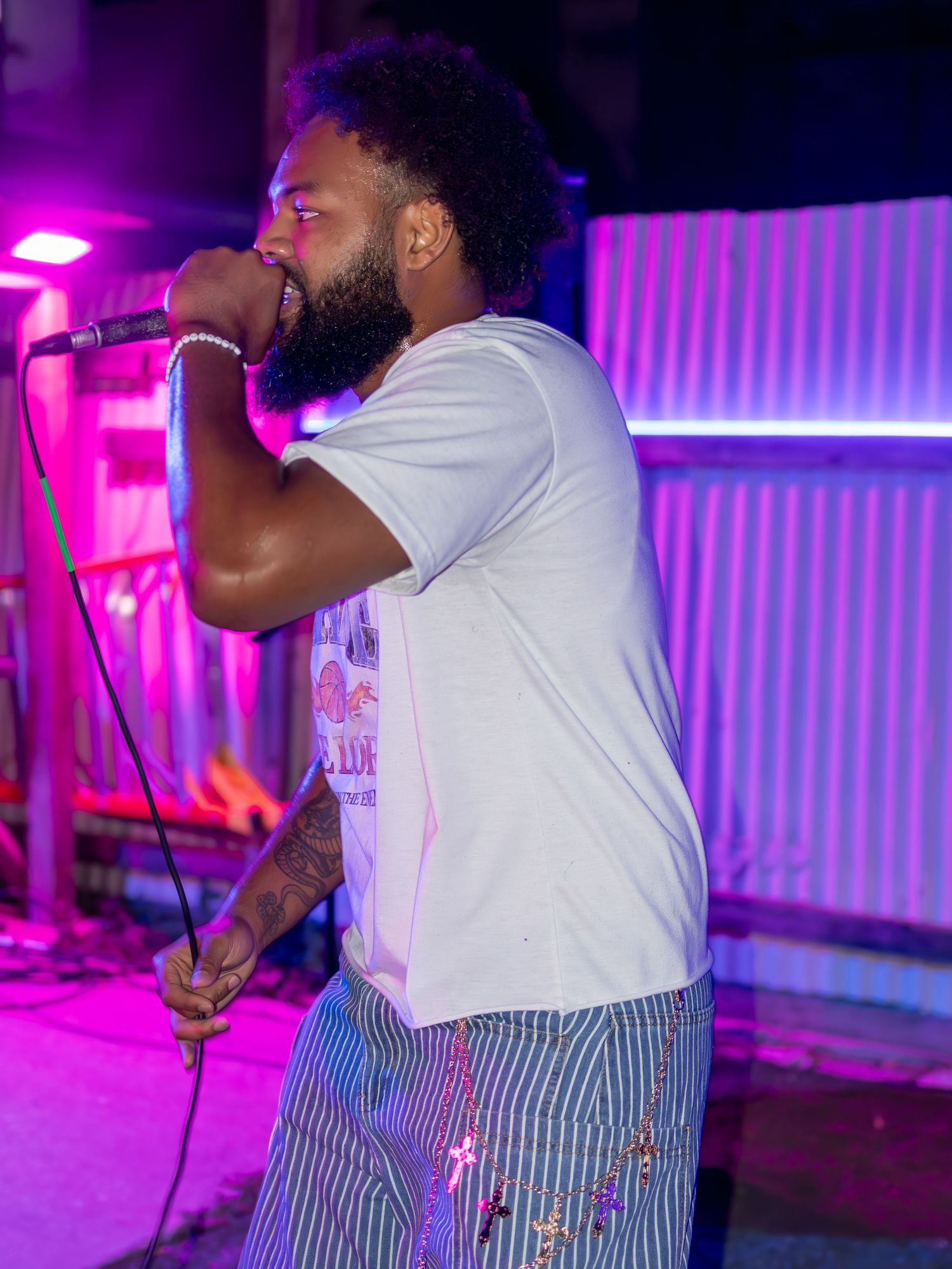 Performer in white t-shirt and striped pants singing on stage with purple lighting effects.