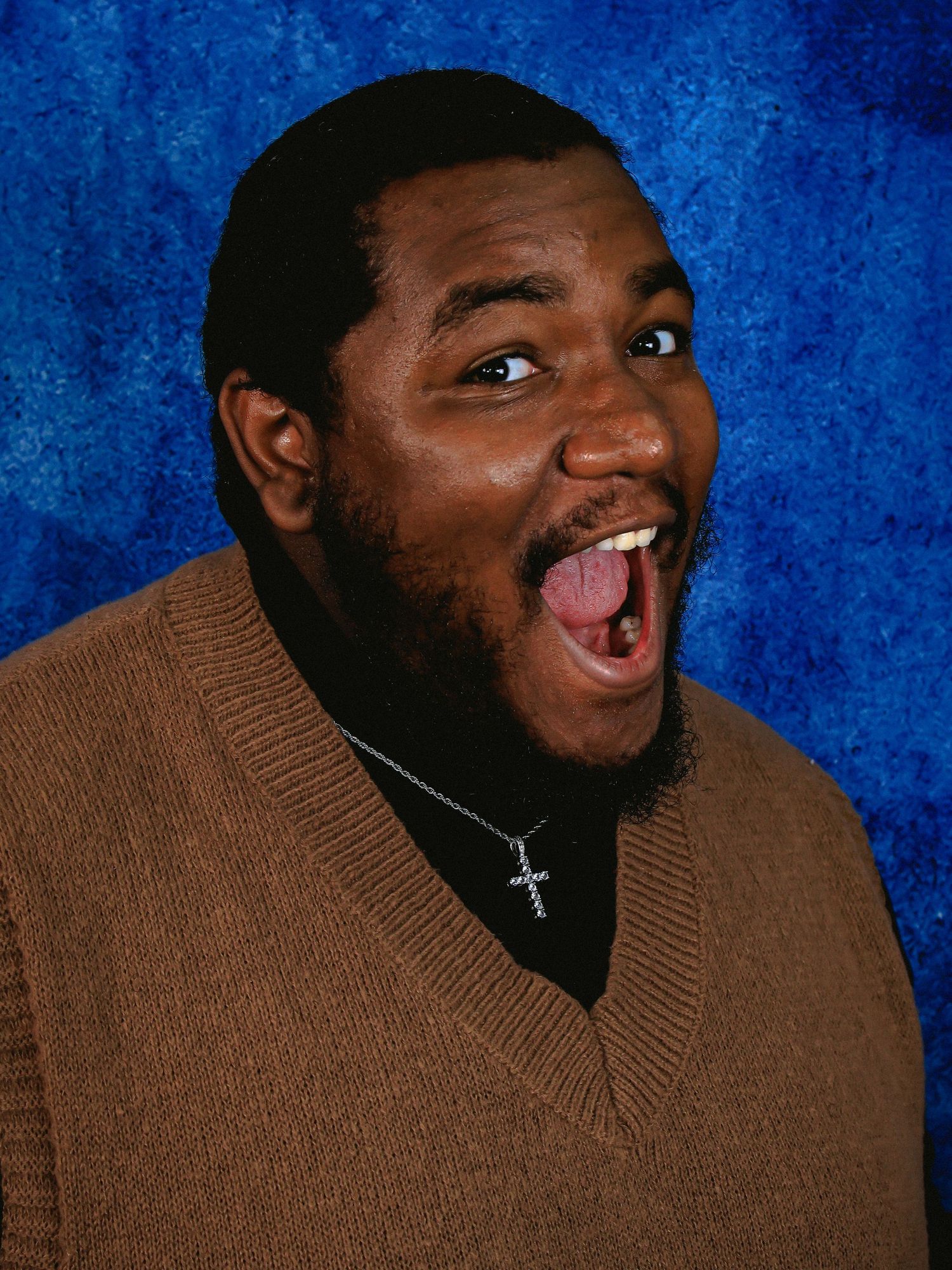 Person in brown sweater making animated expression against blue background.