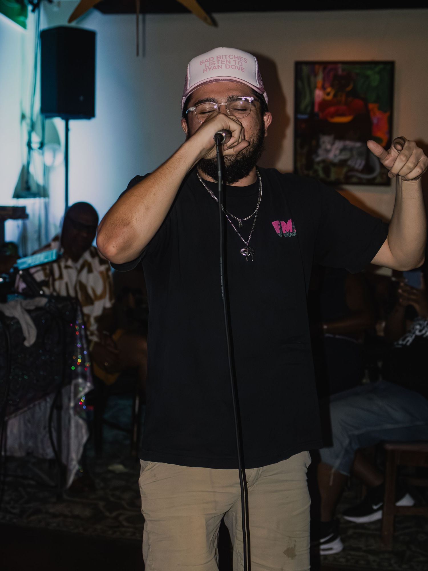 Person wearing a black t-shirt and glasses performs on stage in a dimly lit venue.