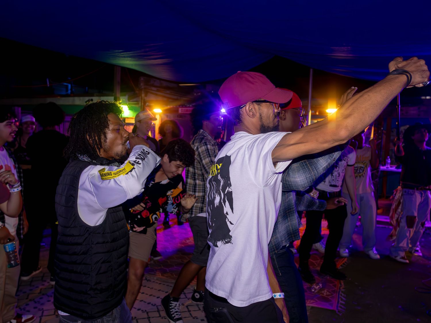 People dancing and raising their arms at an outdoor nighttime music event.
