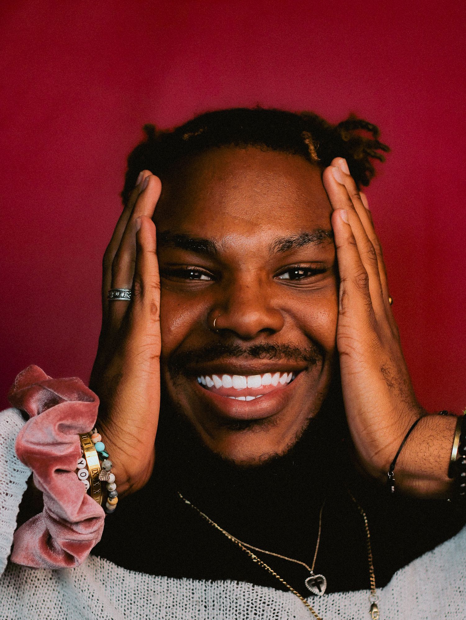 Playful portrait with hands framing face against vibrant red backdrop.