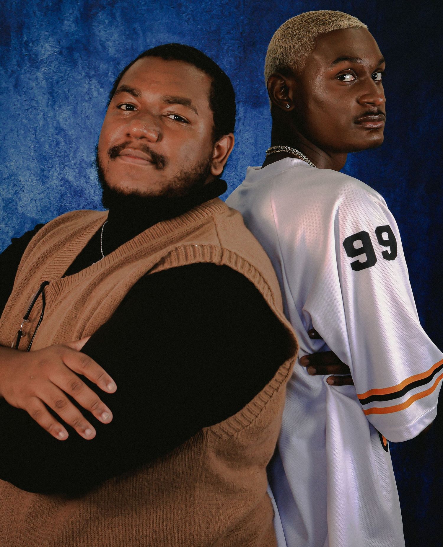 Two figures share an intimate moment wearing contrasting white jersey and brown clothing.