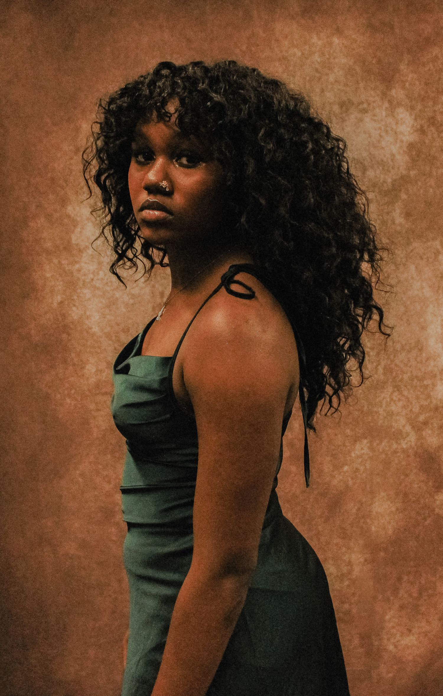 Expressive poses in dark tank top against warm brown studio background.