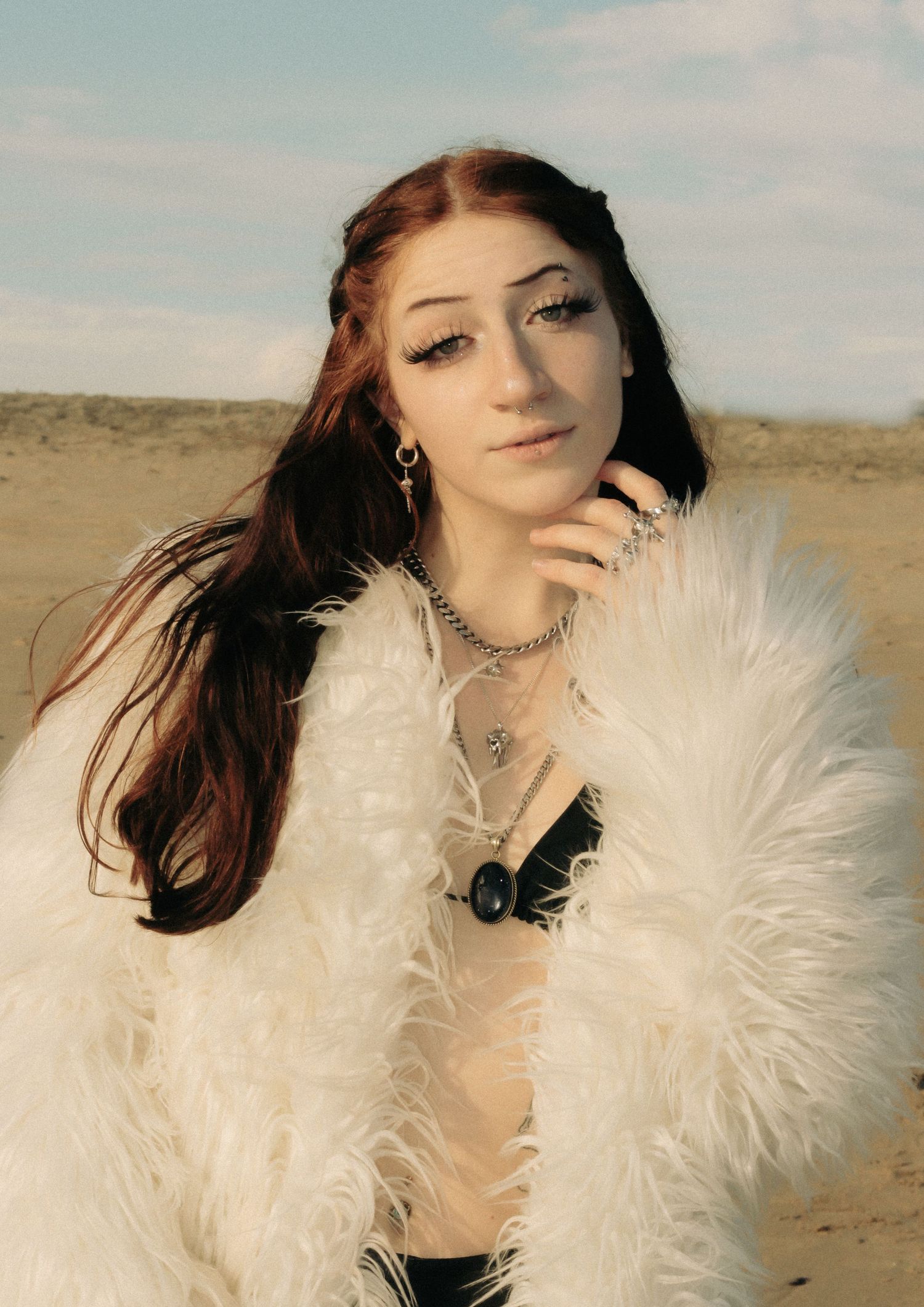 Fashion portrait with white feathered accessory against desert landscape.