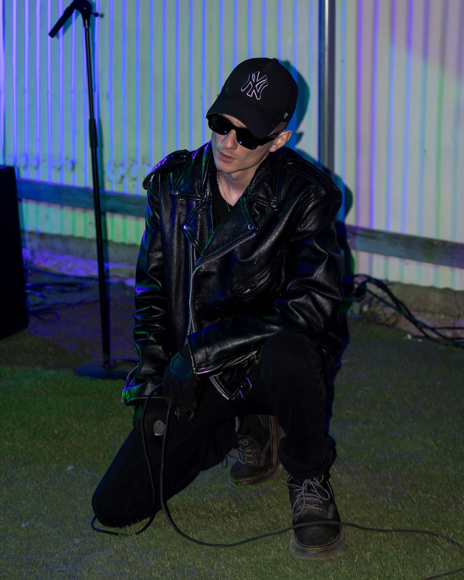 Artist in black attire crouches during performance with vibrant lighting effects.