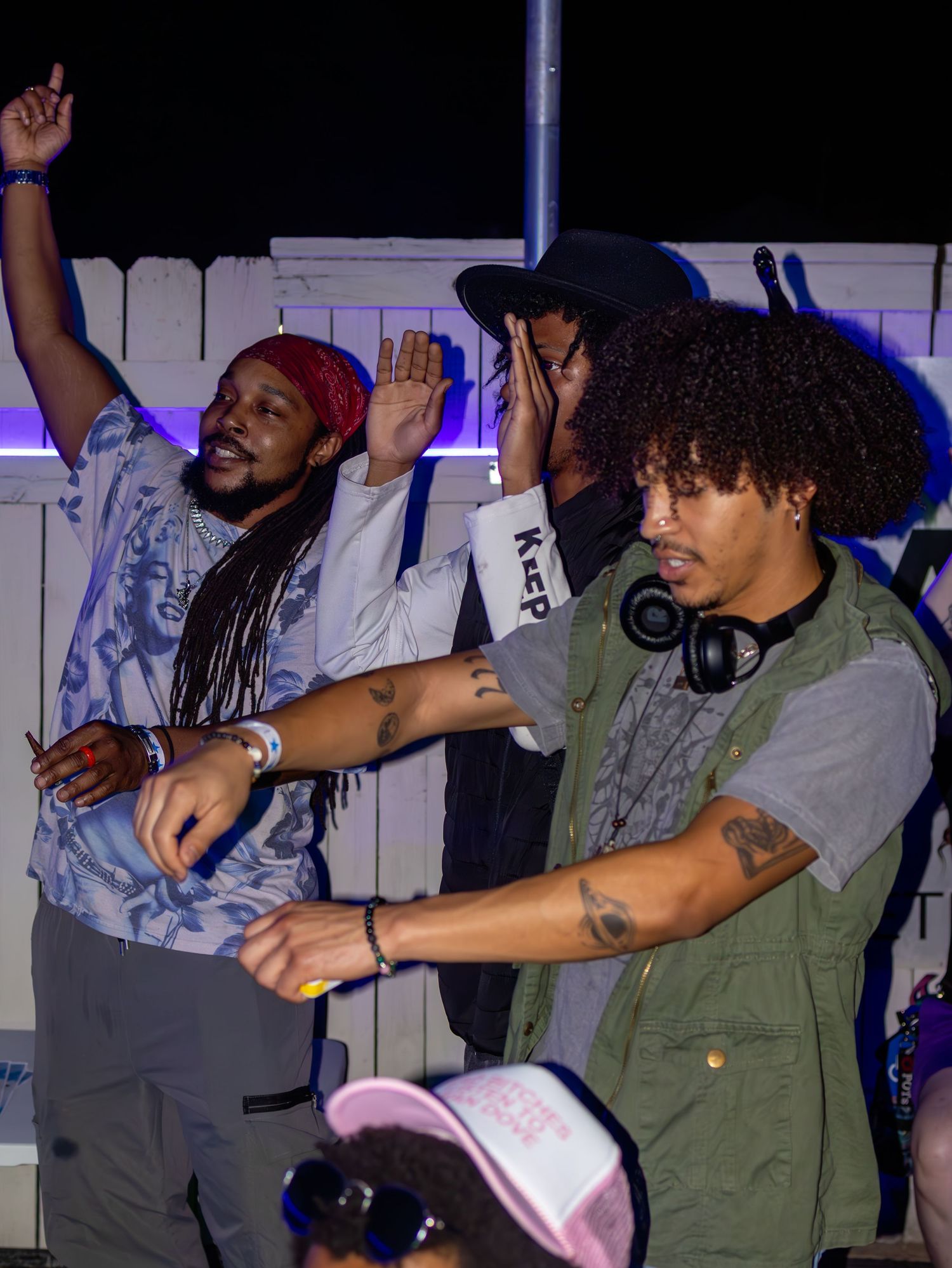 Performers on stage raise their hands during energetic performance with purple lighting.