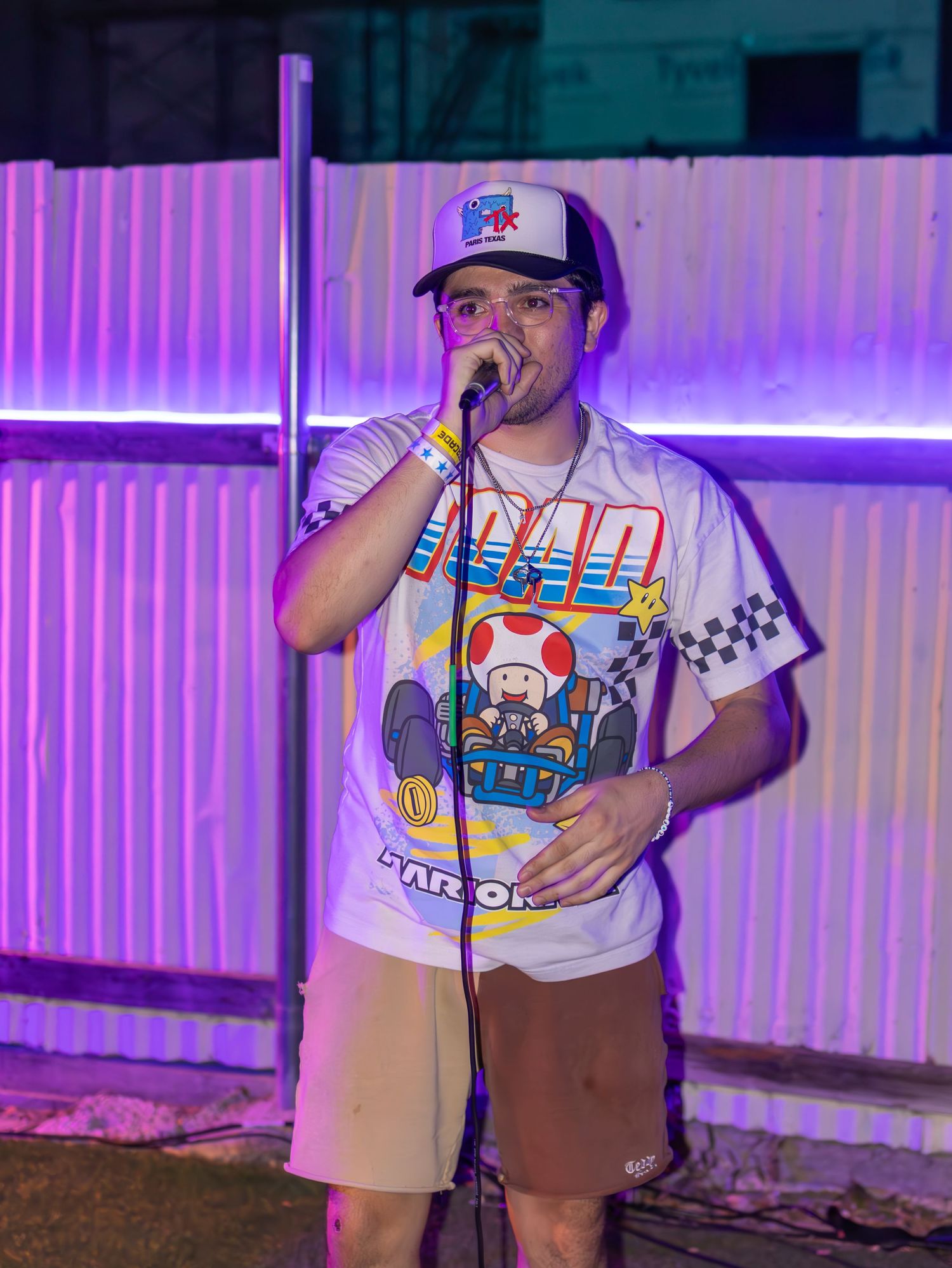 Artist in Mario-themed shirt performing at nighttime venue with purple ambient lighting.