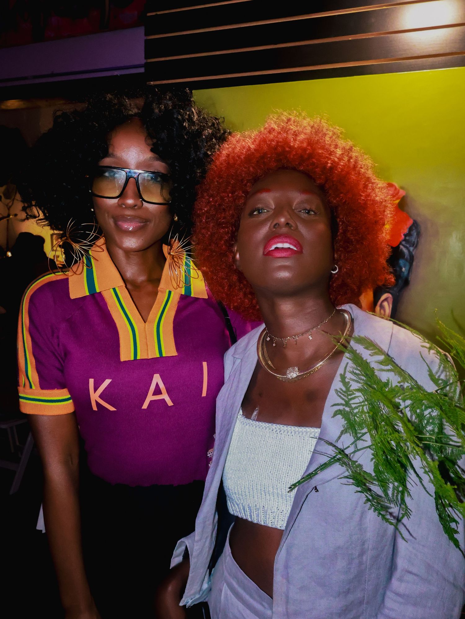 Friends pose for a photo wearing contrasting outfits with a yellow wall backdrop.