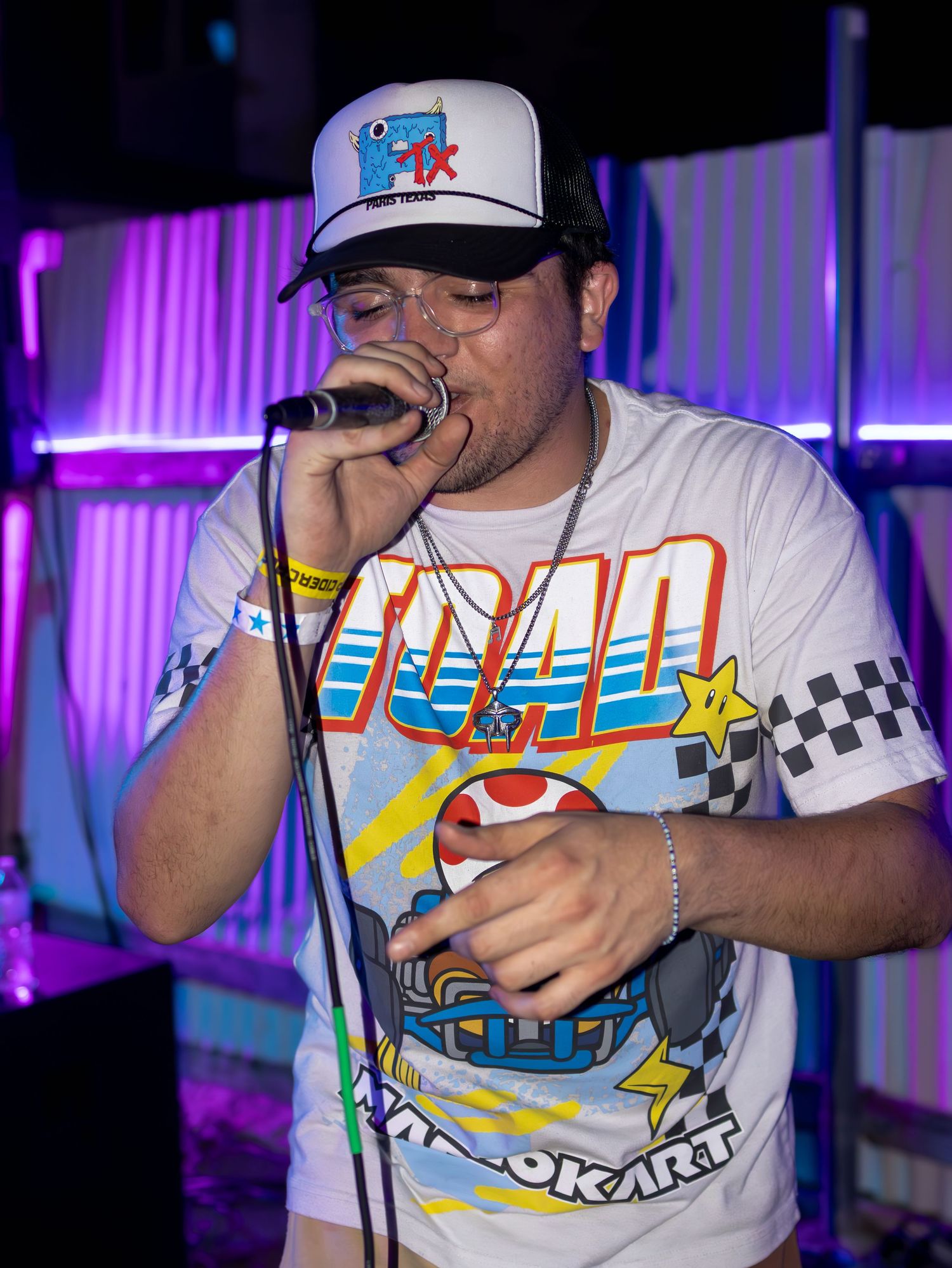 Performer wearing a Mario Kart themed t-shirt and baseball cap singing on stage.