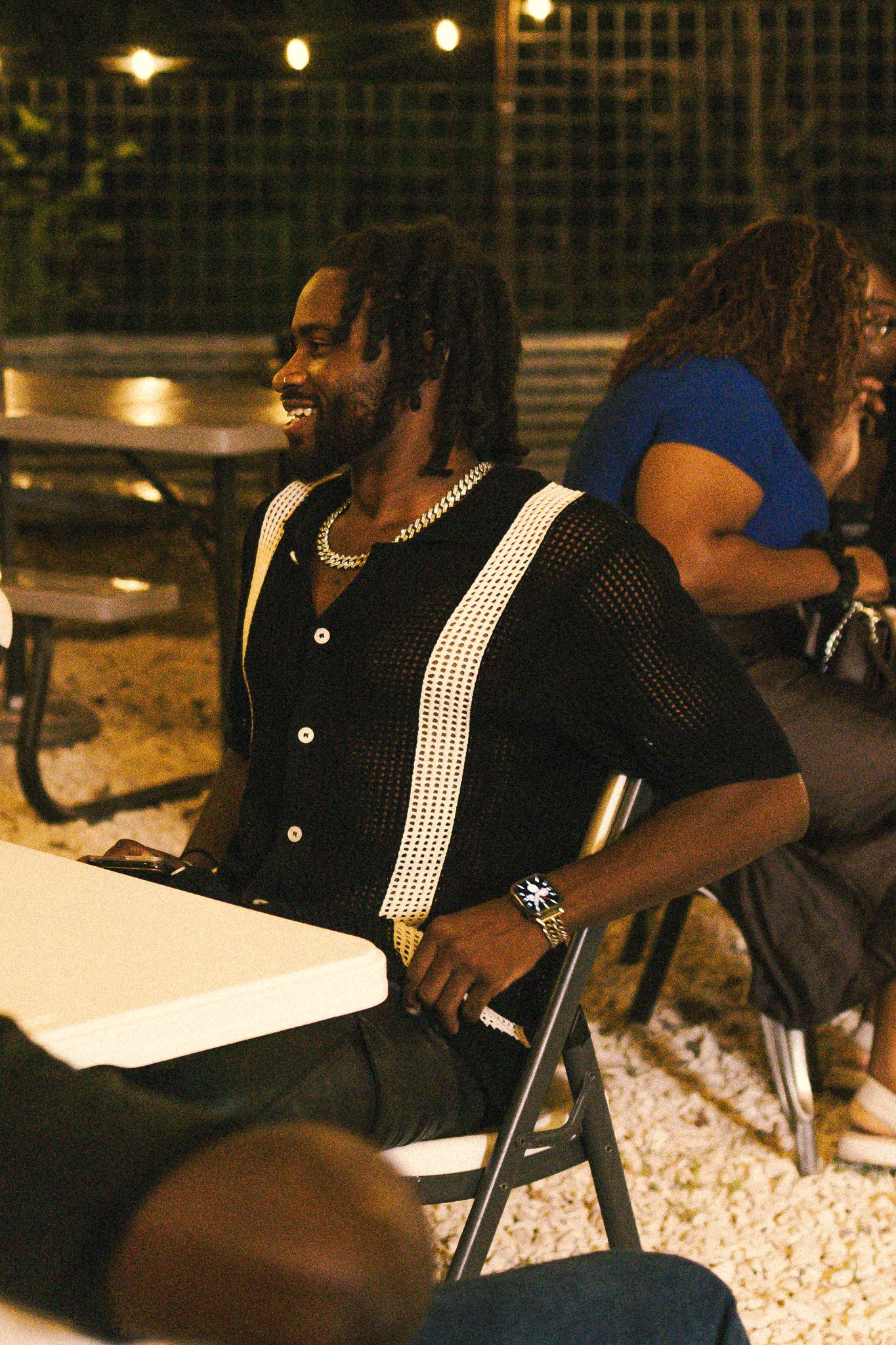 People seated at tables during nighttime outdoor gathering with string lights.