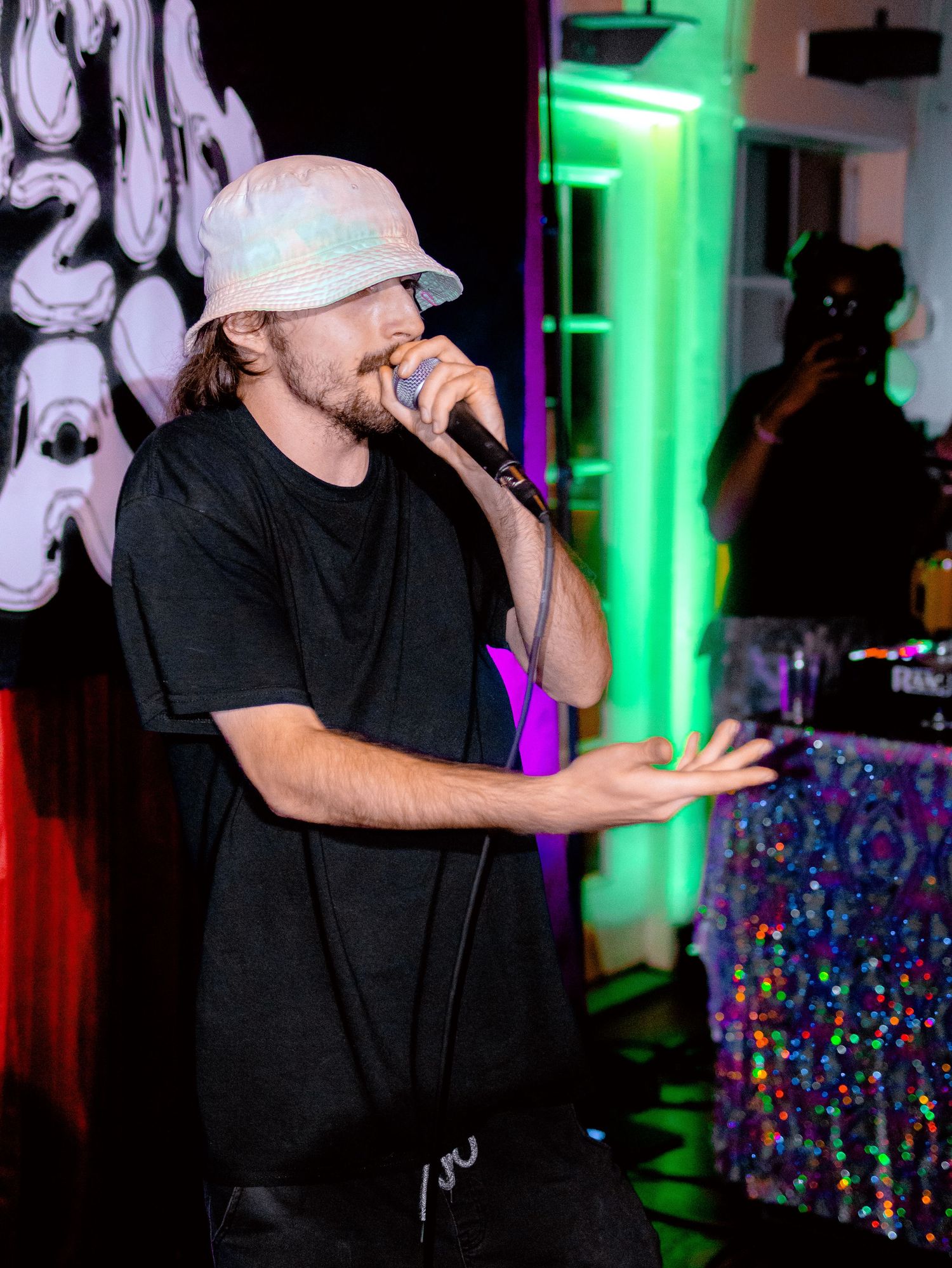 Performer in black outfit and cap delivering energetic performance with dramatic stage lighting.