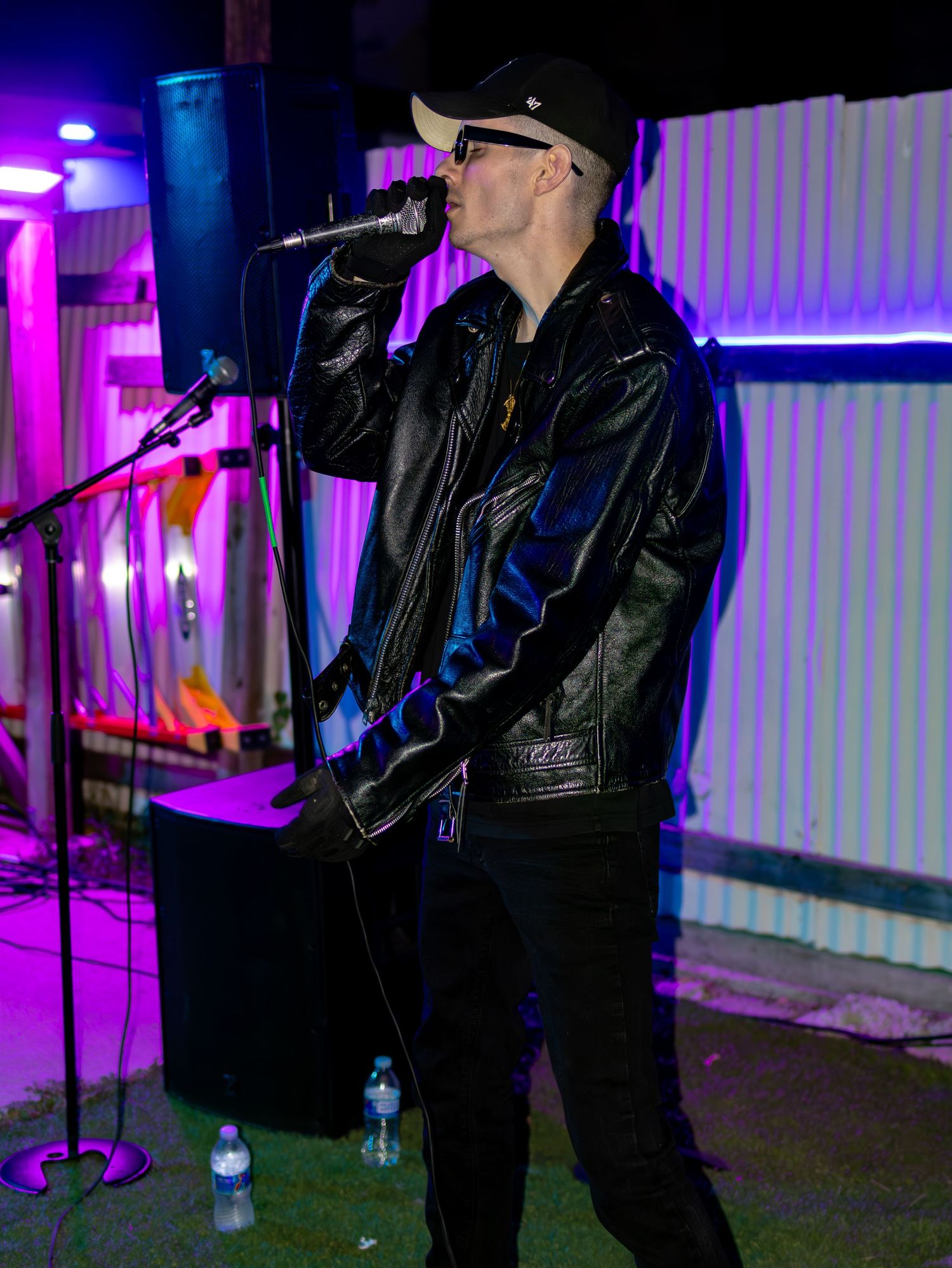 Performance shot of singer in black outfit with neon pink and blue lighting effects.