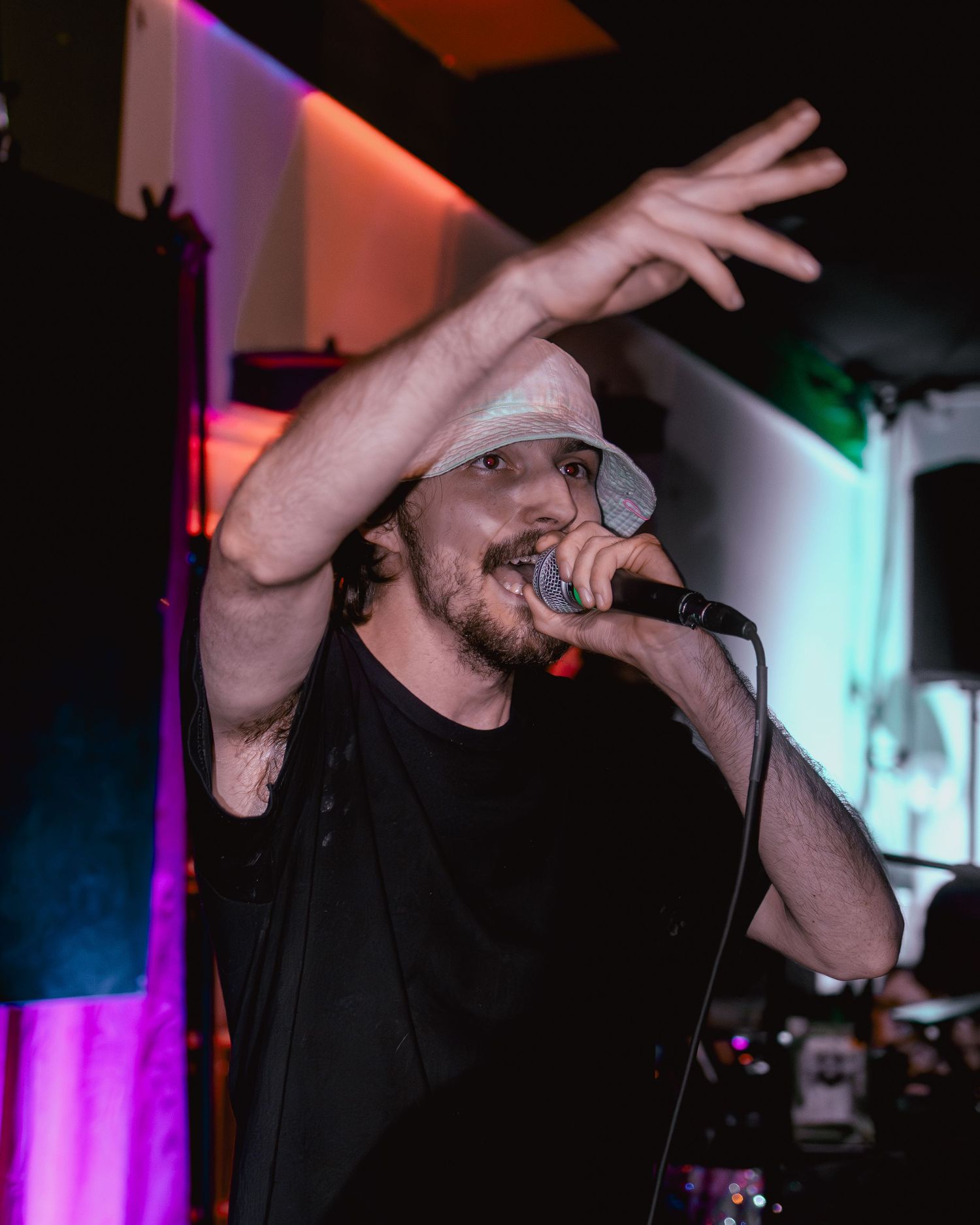 Rapper in dark attire performing with expressive hand gestures under stage lighting.