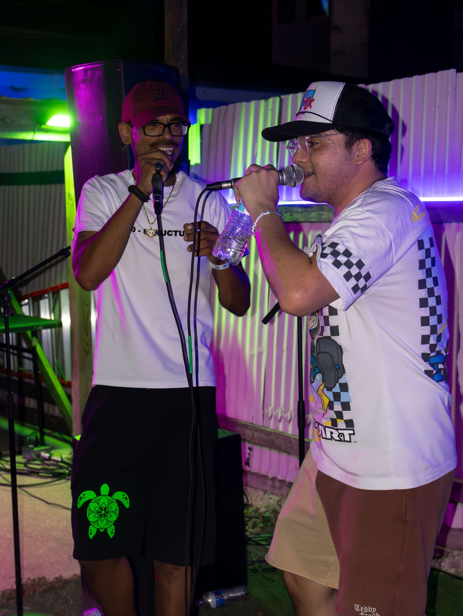 Musicians performing under purple and green stage lights at a nighttime venue.