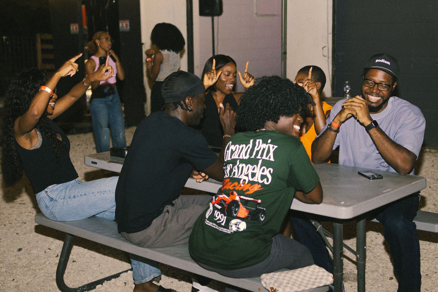 Group seated at tables during a nighttime outdoor event with string lights.