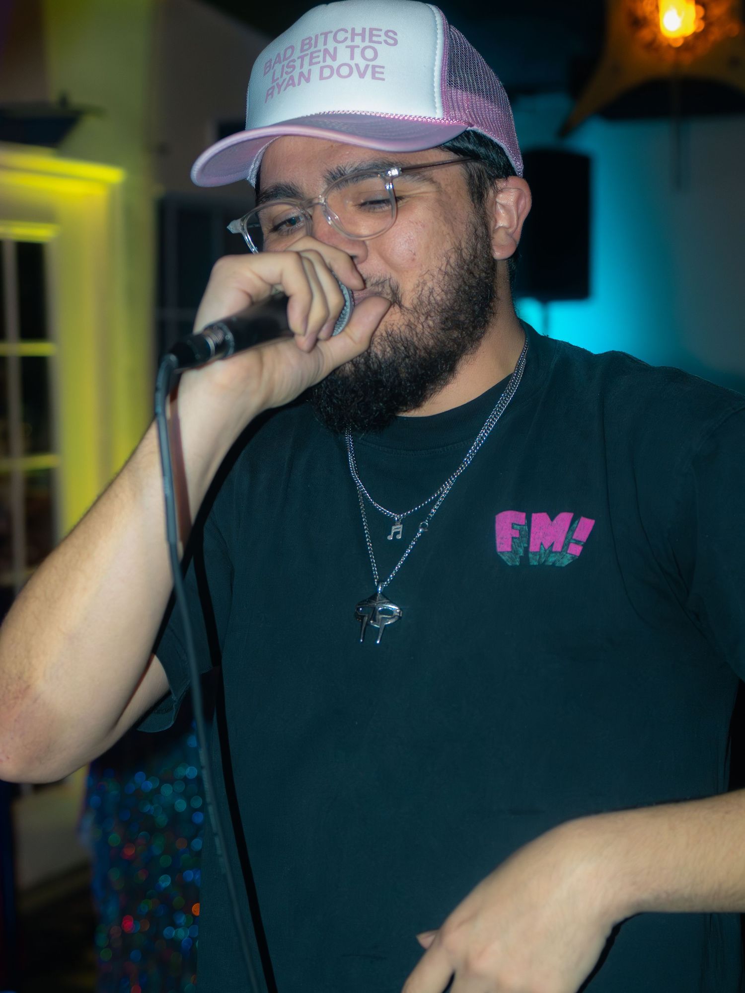 A performer in a black shirt and pink cap energetically delivers lyrics into a microphone.