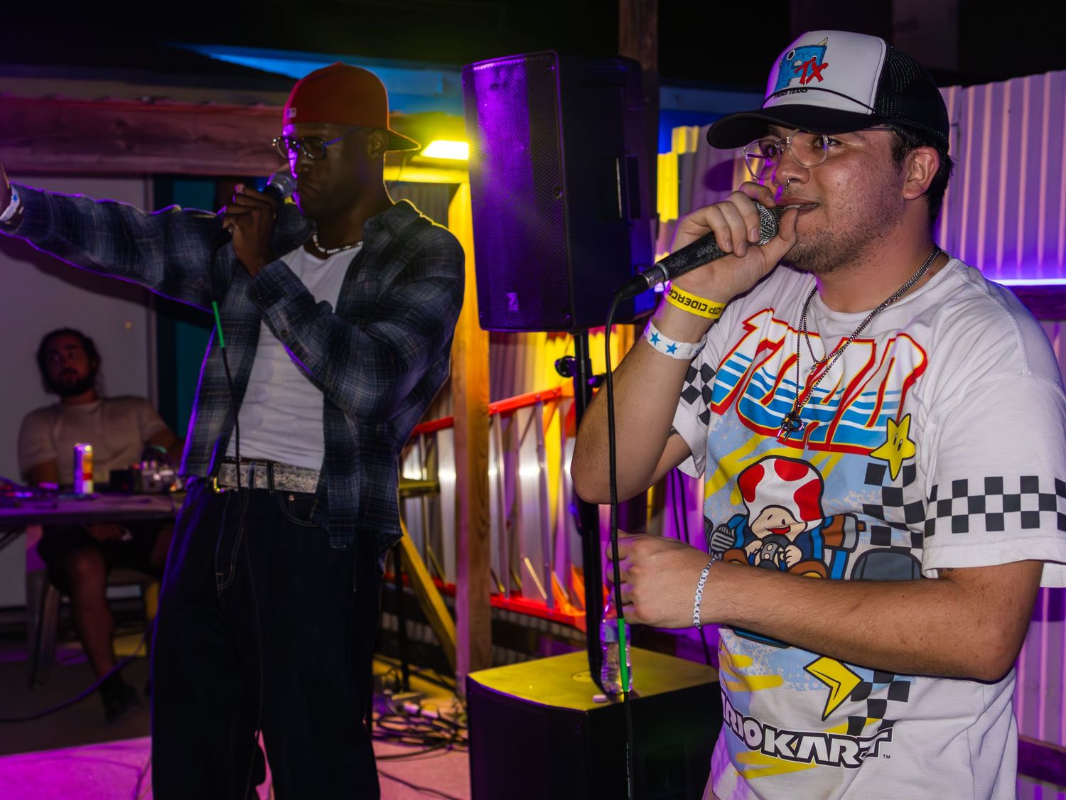 Musicians on stage at venue with checkerboard themed shirts and vibrant lighting effects.