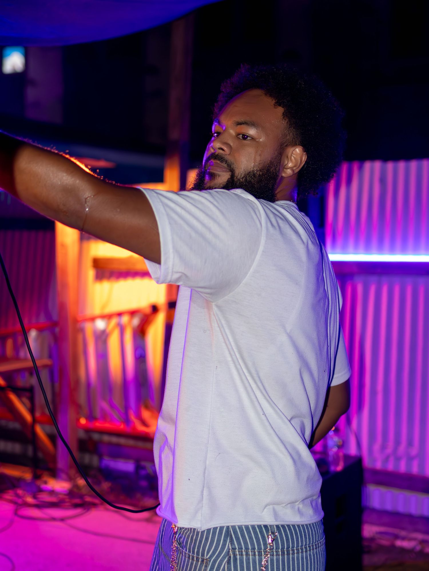 Musician gesturing with arms raised during live performance with colorful stage lighting.