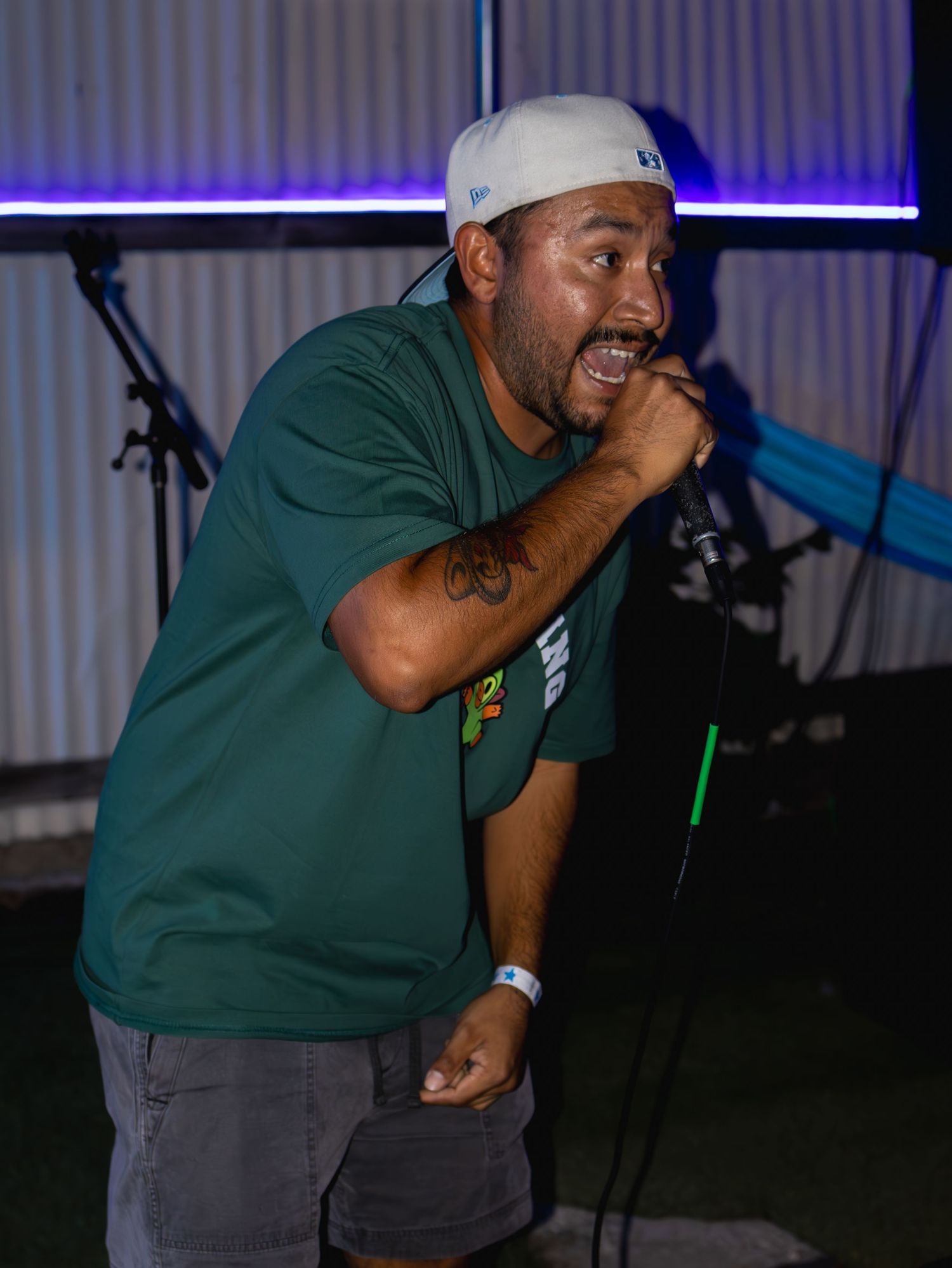 Performer in green shirt and white cap shows emotion while holding microphone during show.