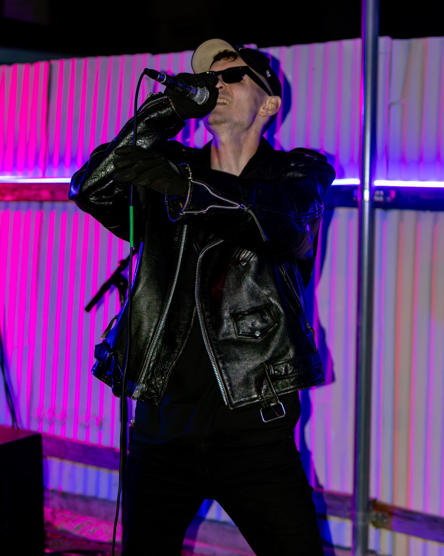 Performer in dark outfit and cap sings against purple-lit backdrop during show.
