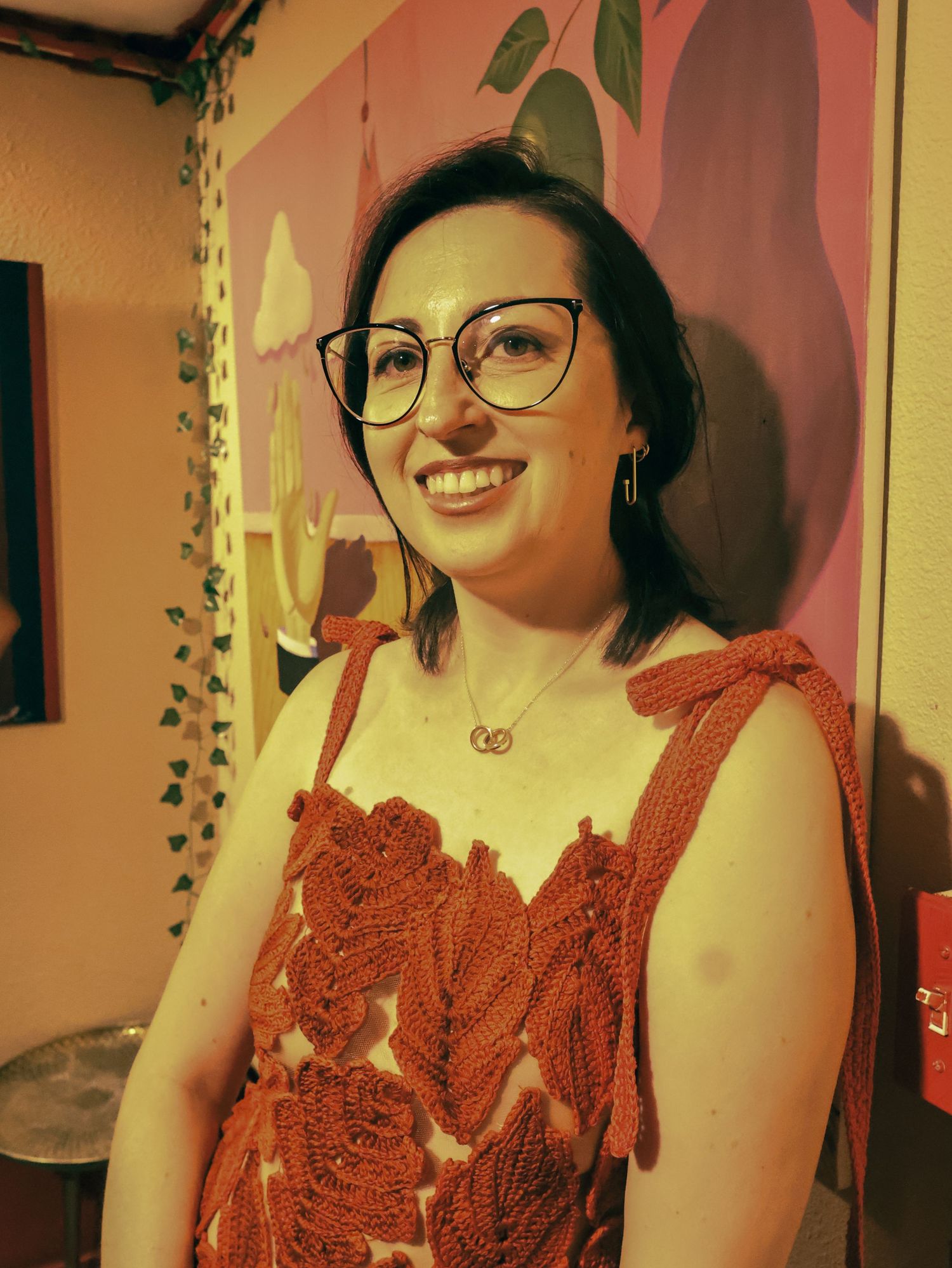 A red crochet dress with delicate patterns is displayed in warm lighting against a beige wall.