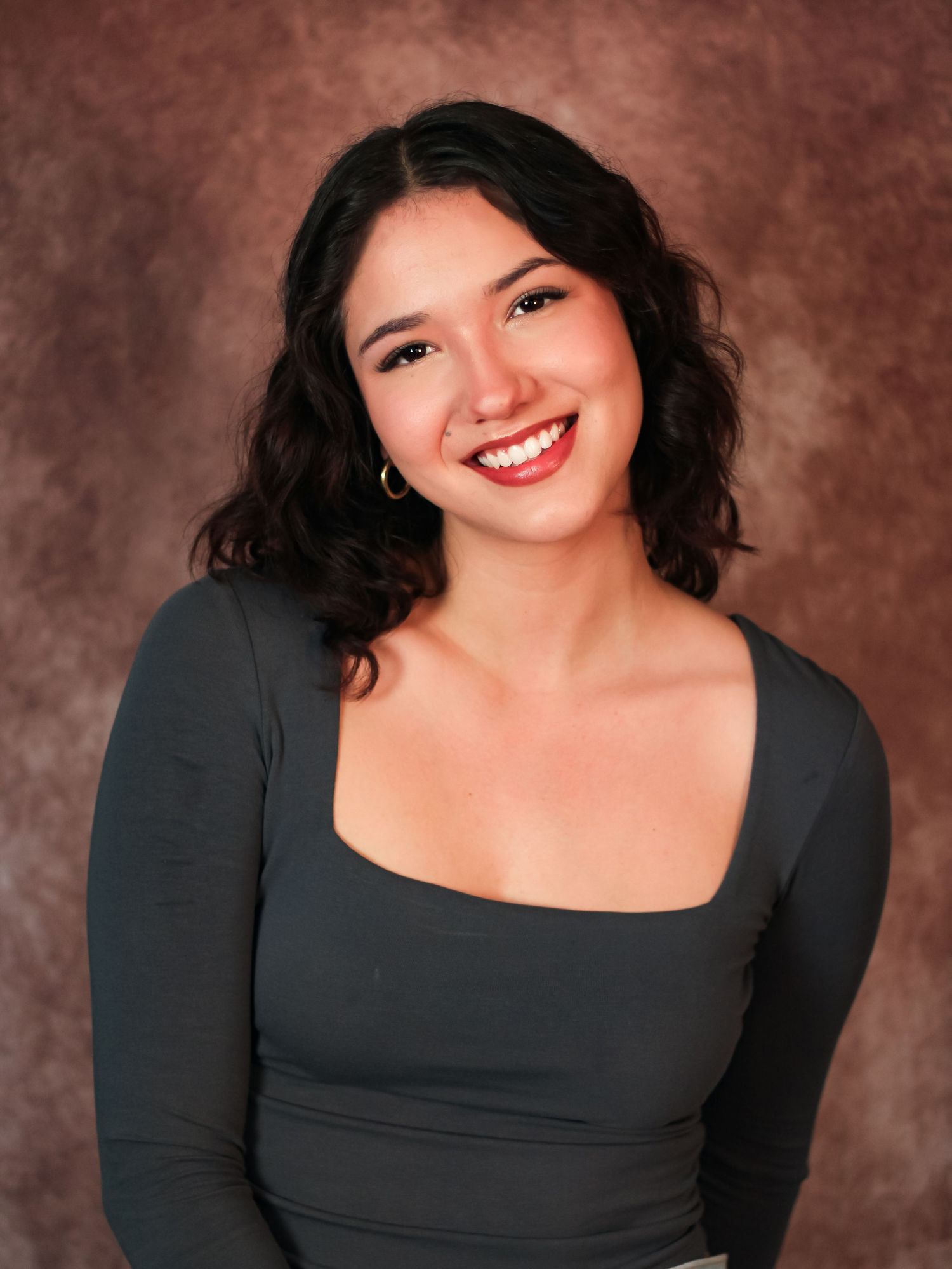 Studio portraits in black top against textured brown backdrop with warm lighting.