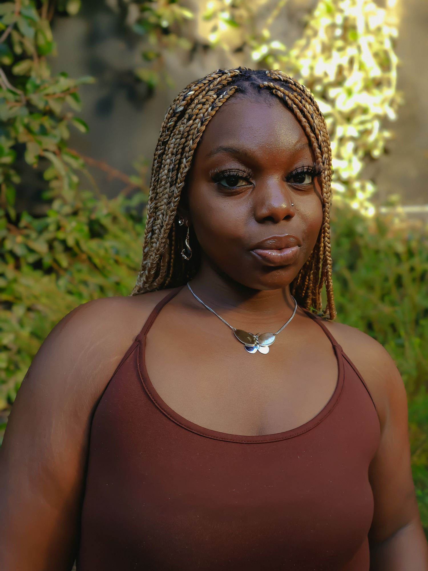 Portrait shot in natural lighting with greenery and sunlit background.