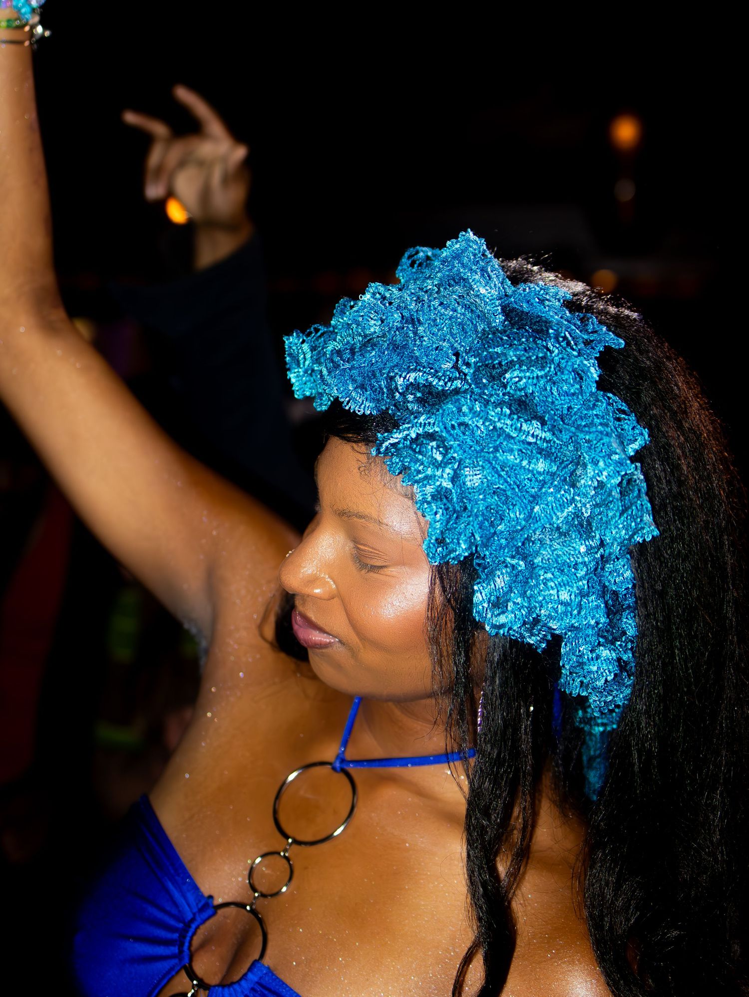 Dancer with bright blue hair accessory performing energetically in dark venue.