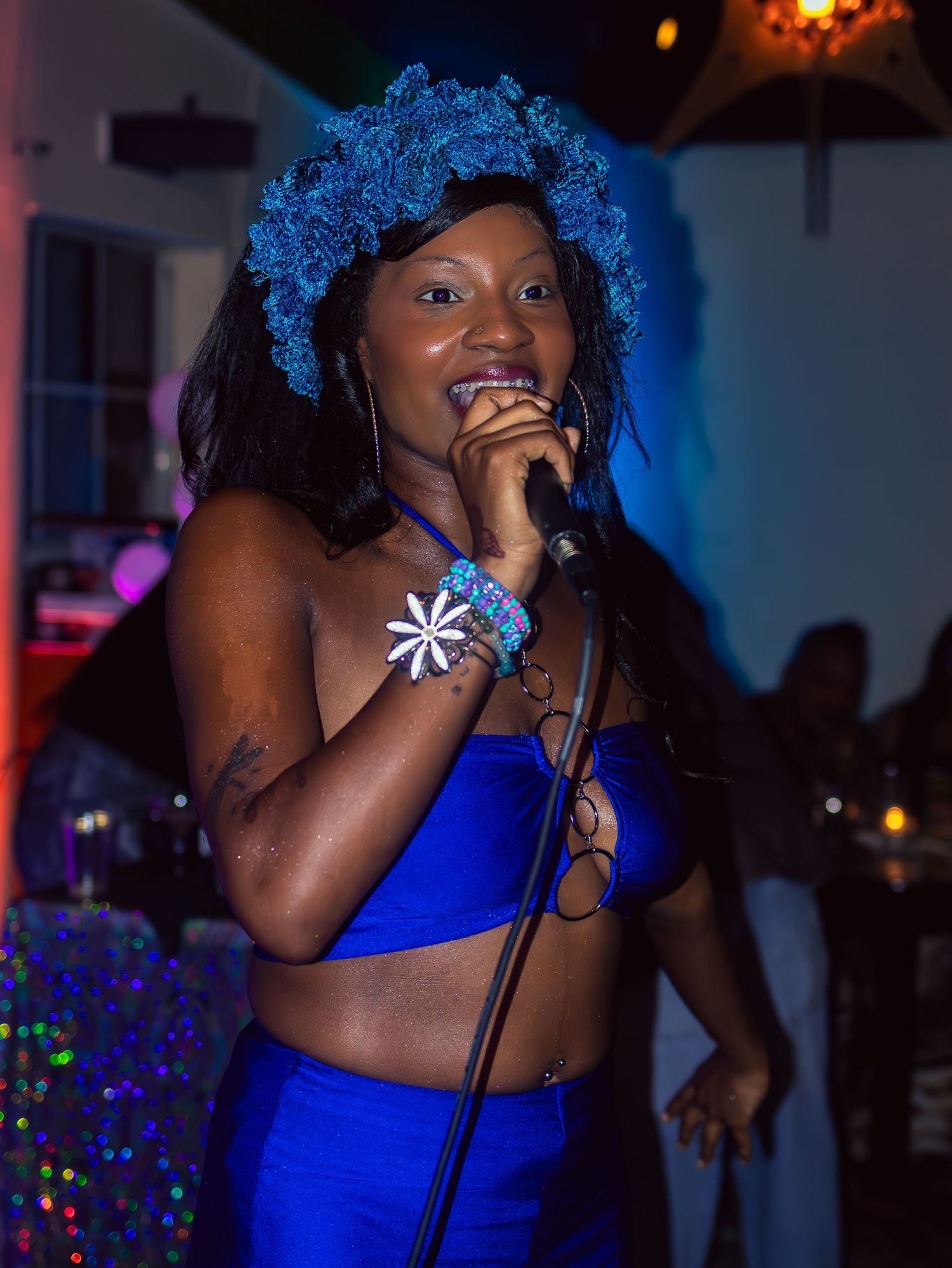 Singer in vibrant blue attire and blue wig performs passionately on stage.