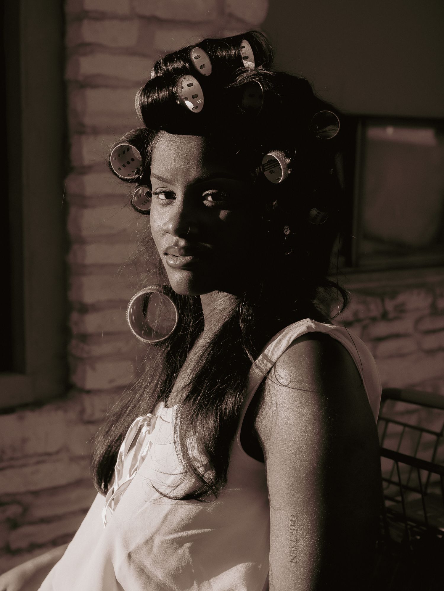 Black and white portrait showing model with hair in curlers wearing light dress.
