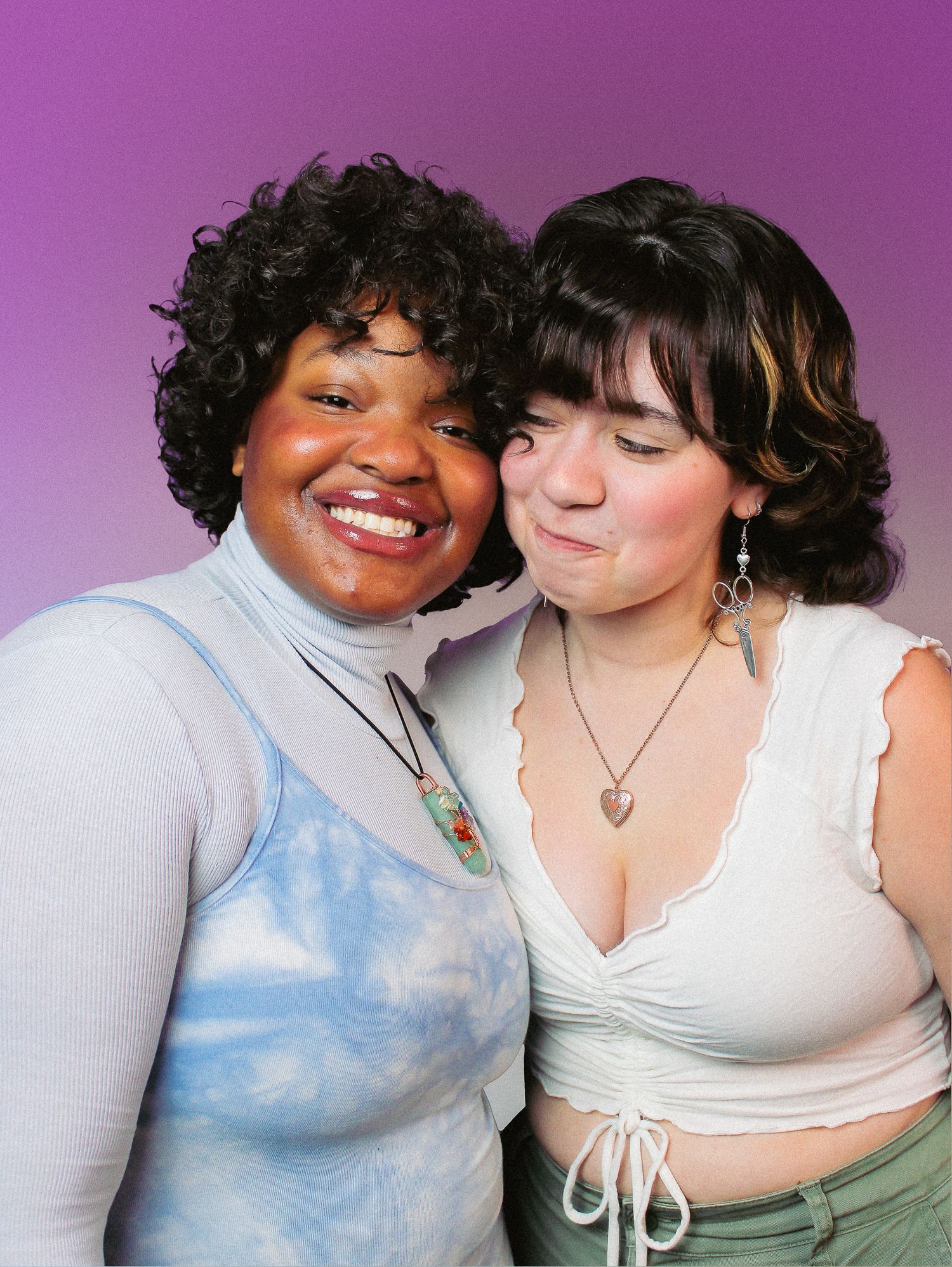 Two young women smiling and posing together against a purple gradient background.