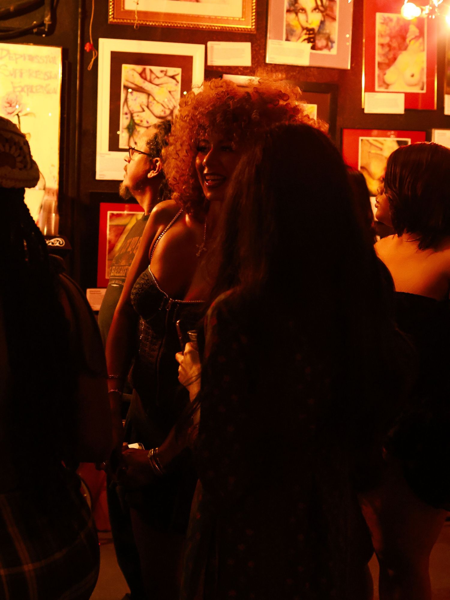 People silhouetted against warm lighting and framed photographs on a wall.