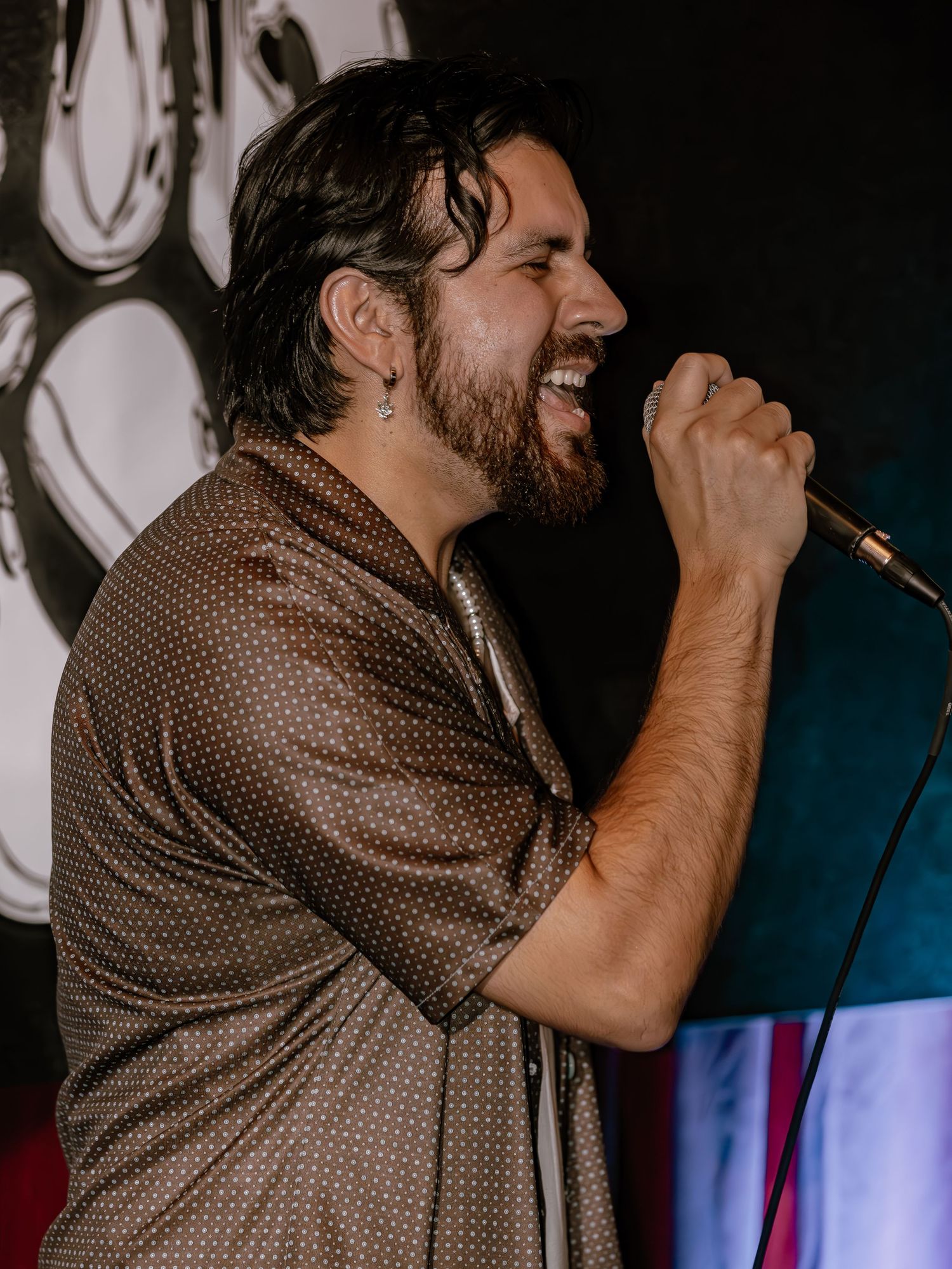 Concert performer in polka dot shirt delivers animated vocal performance on stage.