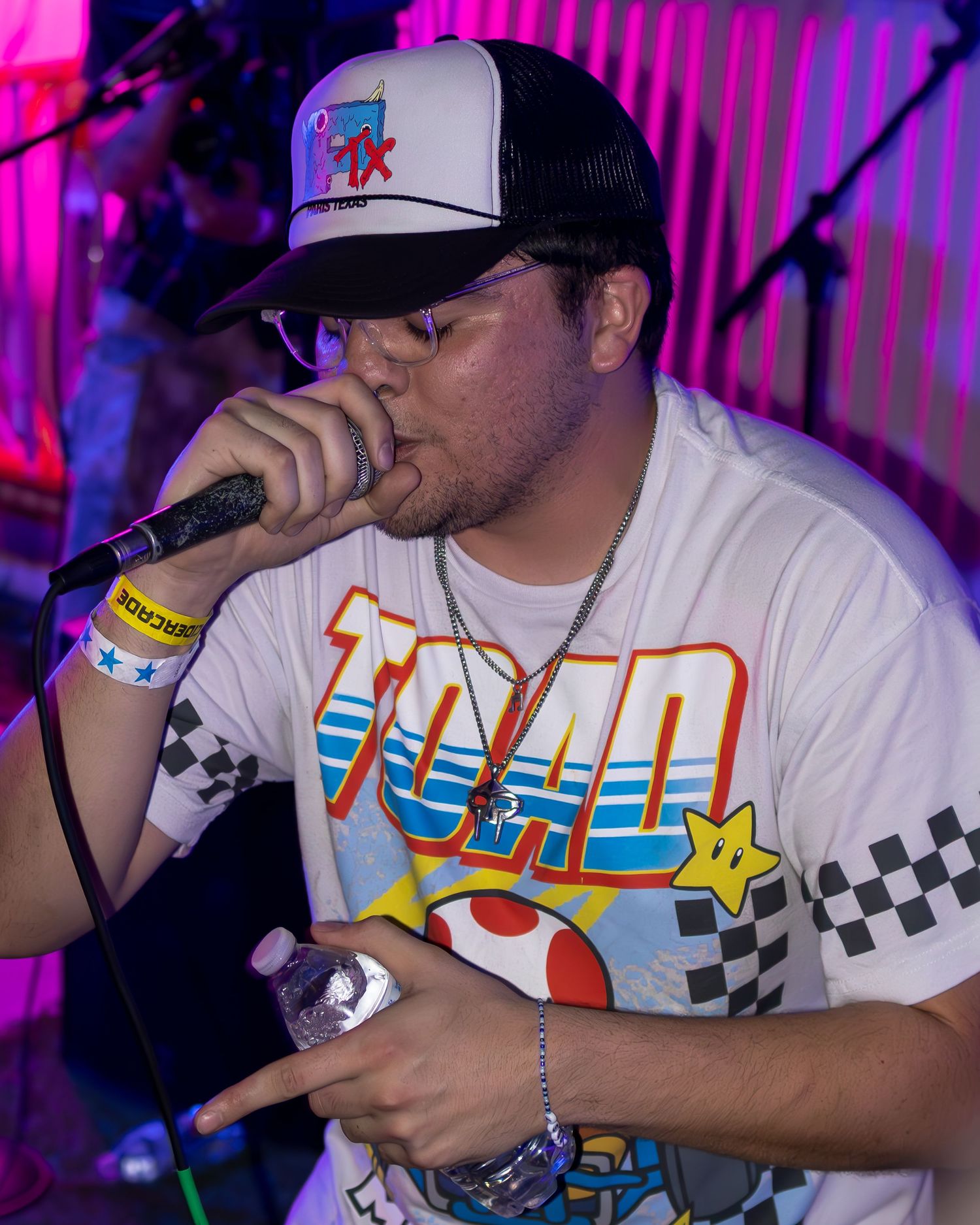Singer in Mario Kart themed shirt performing at venue with purple ambient lighting.