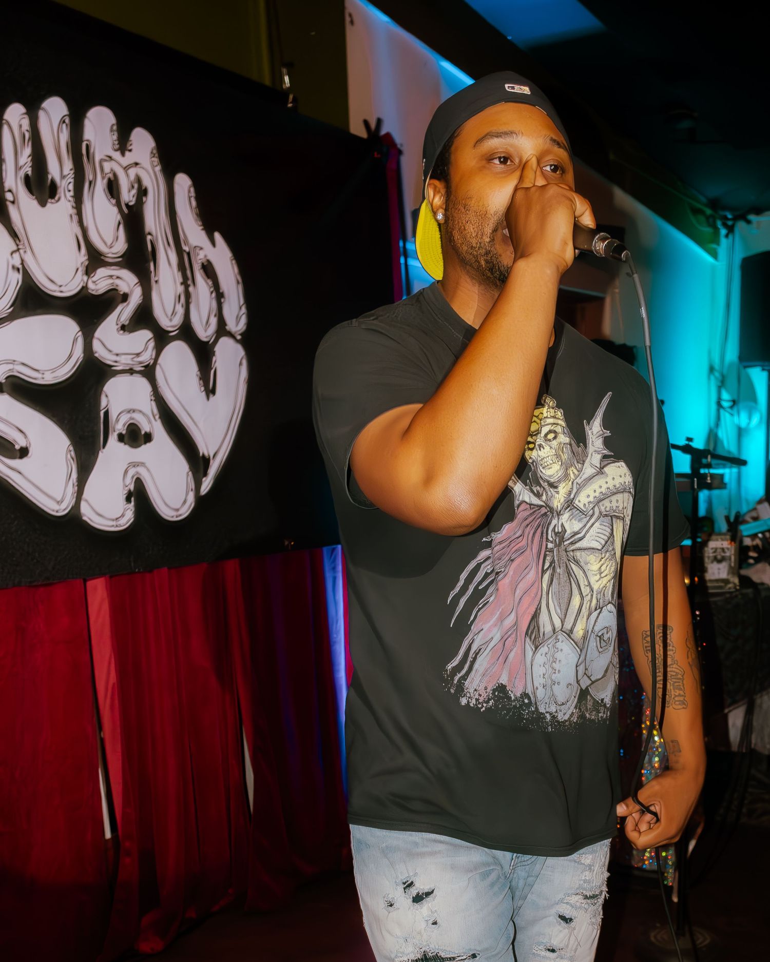 Rapper in graphic t-shirt performs against backdrop of graffiti-style wall art under stage lighting.
