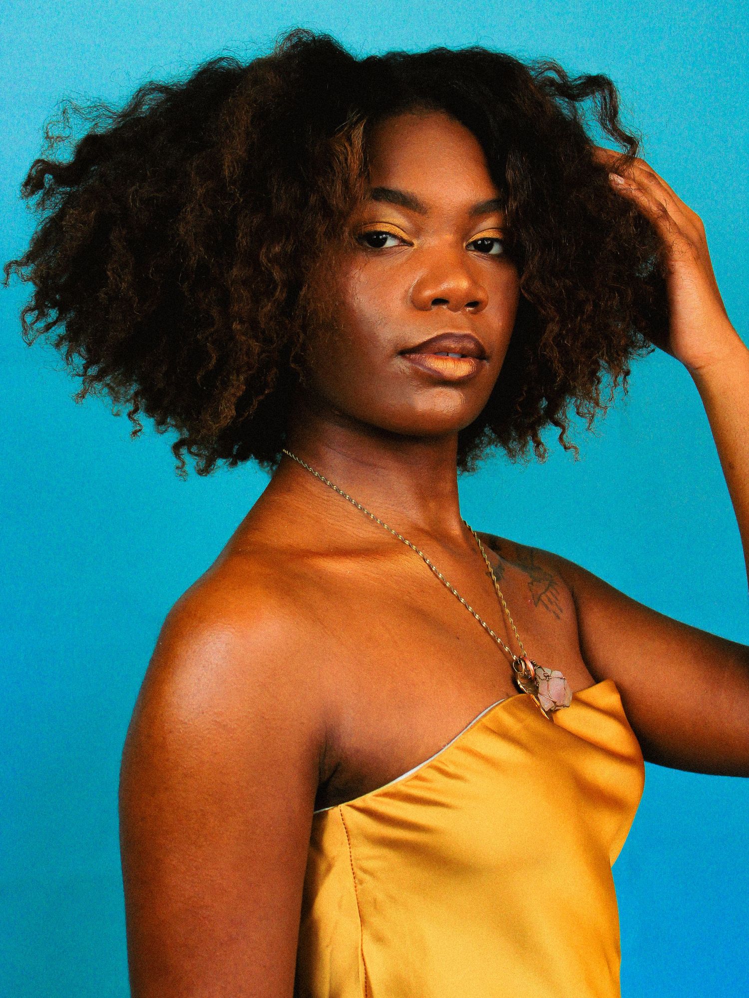 Fashion portrait showcasing natural hair and gold dress against bright blue backdrop.