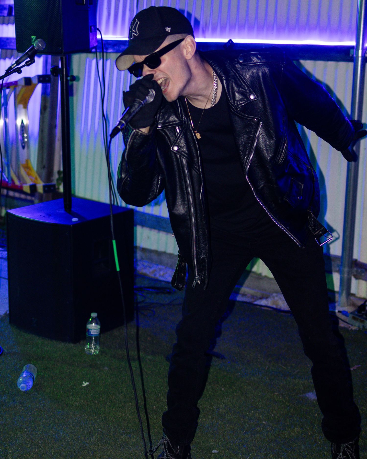 Performer in black leather jacket and cap singing with dramatic stage pose.