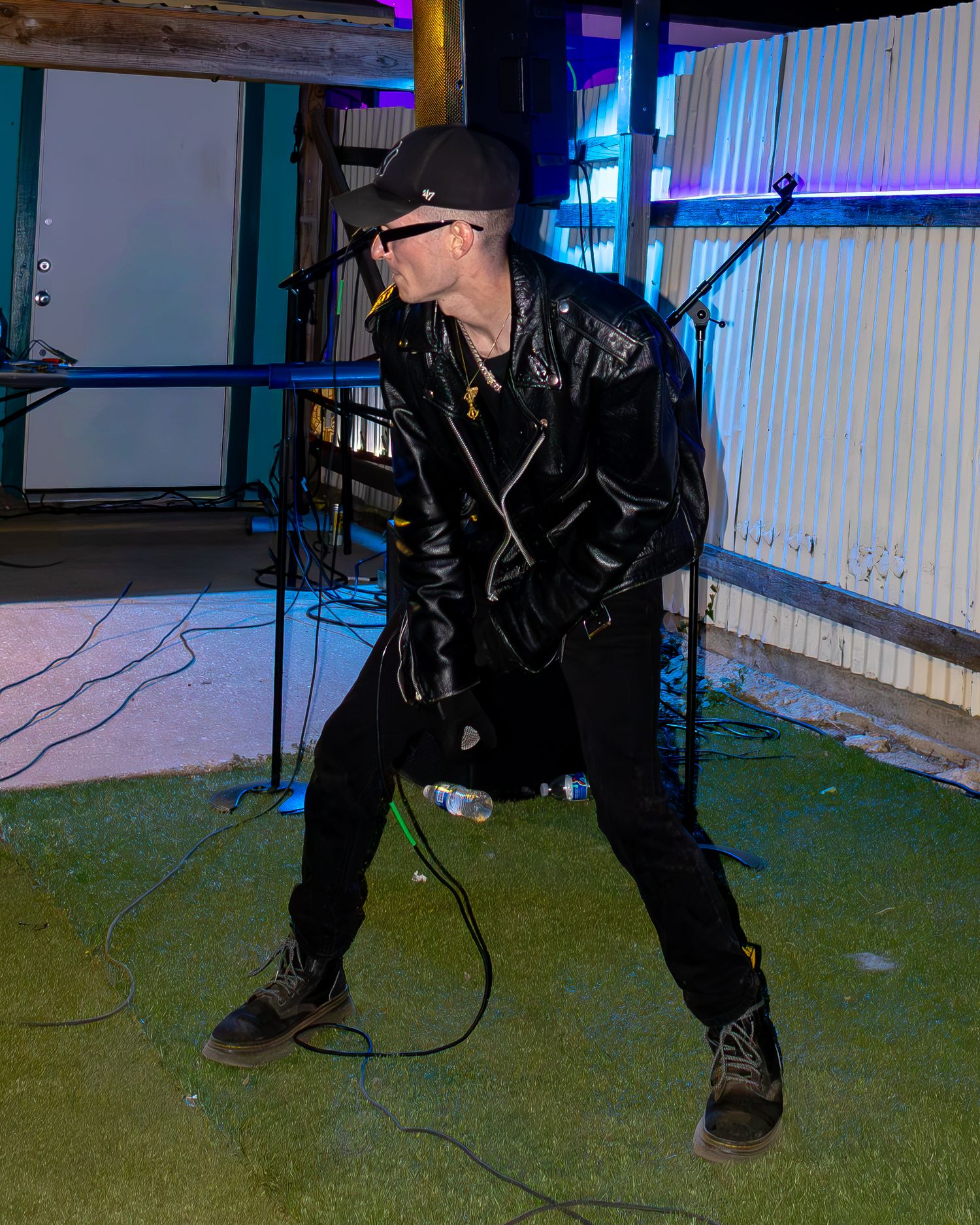 Performer in dark clothing on stage with dramatic lighting and microphone setup.