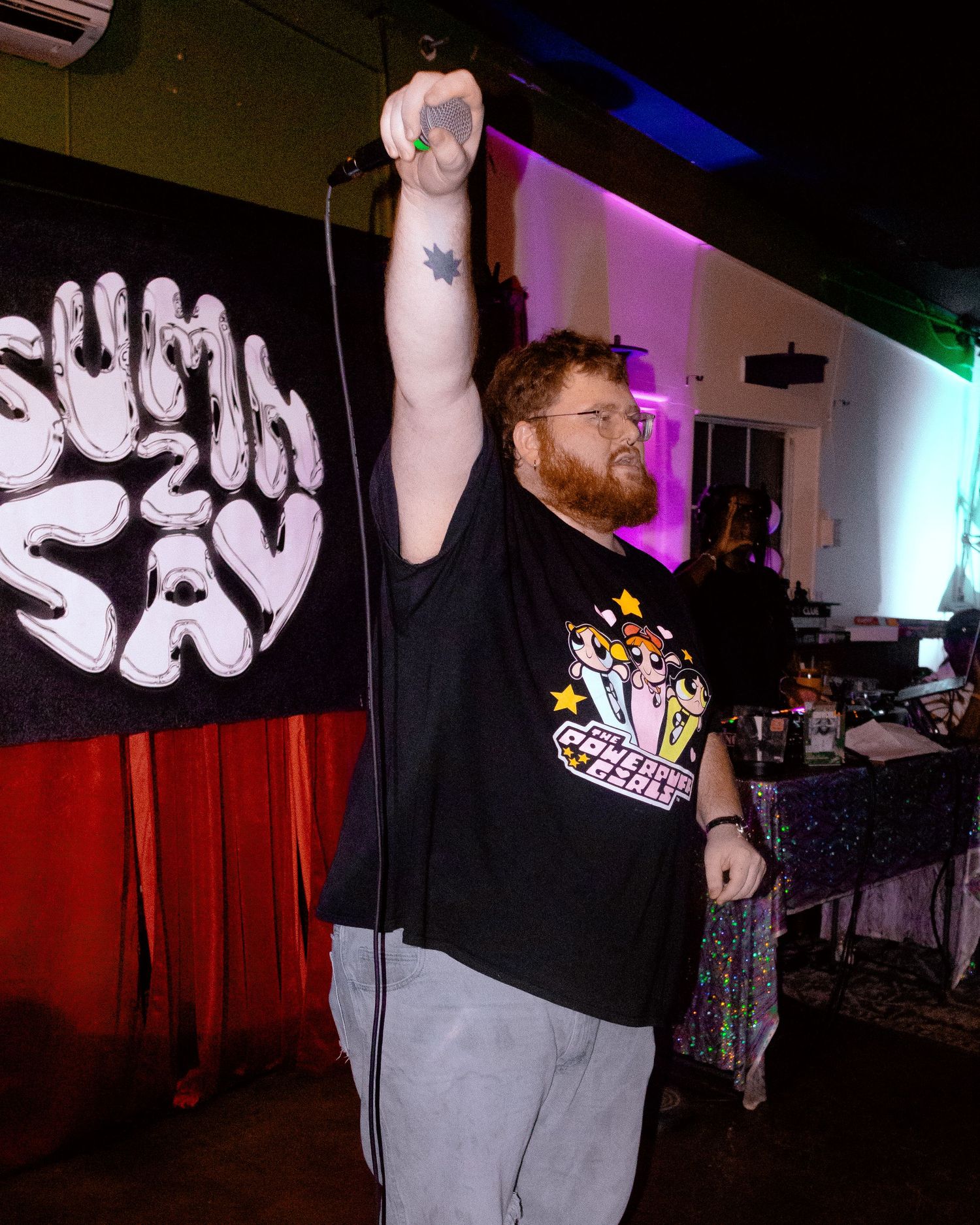 Artist performing on stage with dramatic lighting and a black backdrop with white text.