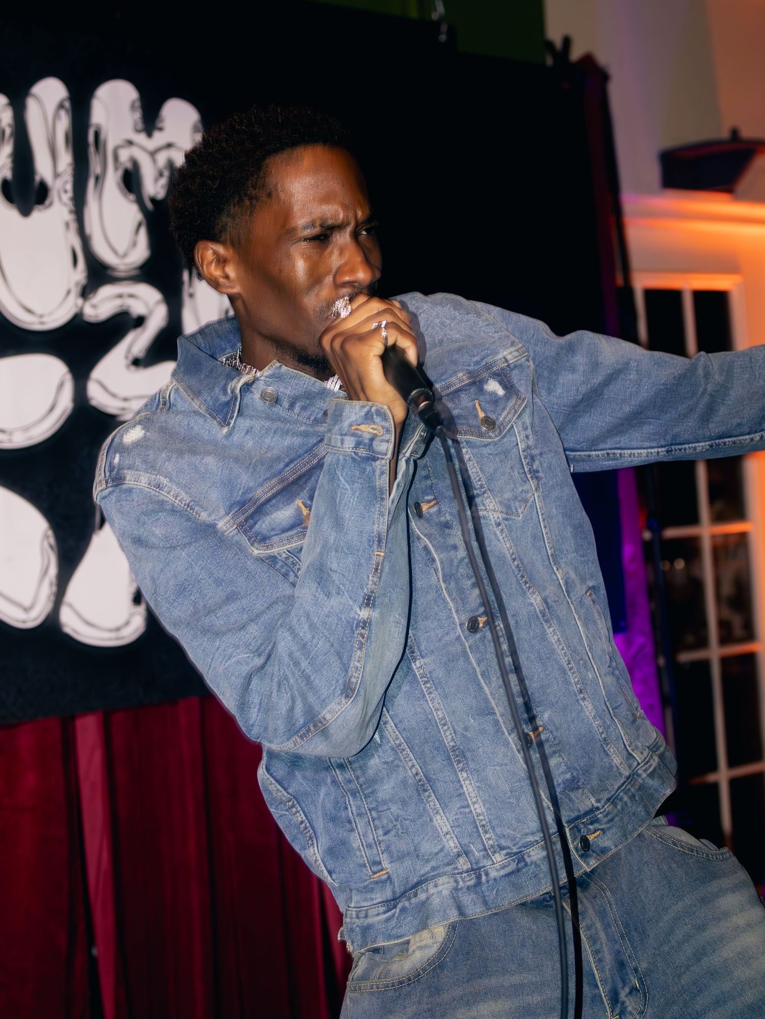 Artist in full denim ensemble performing with expressive movements against purple and orange stage lights.