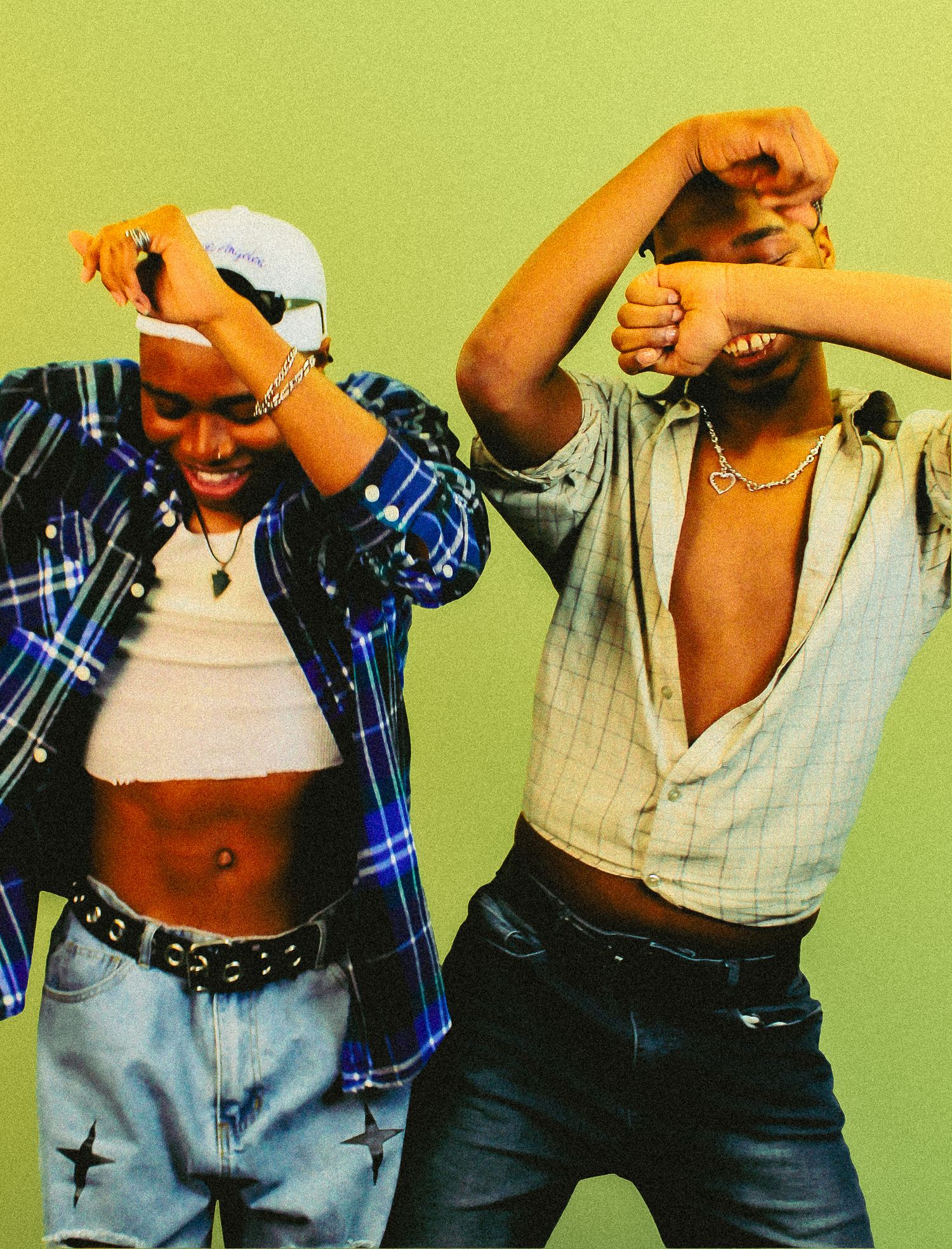 Two stylish young people dance together wearing open flannel shirts and jeans against green background.