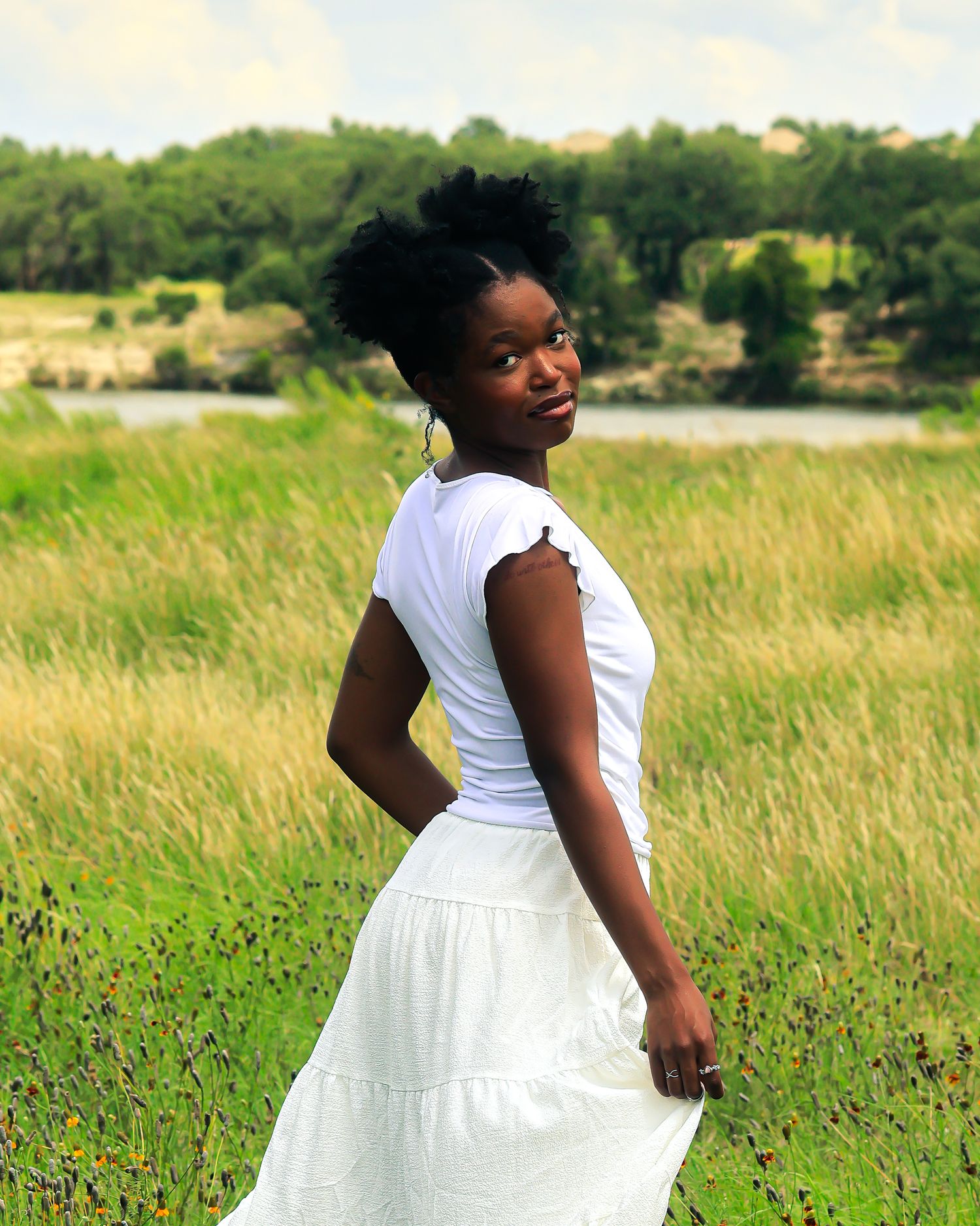 A white sundress flows gracefully in a meadow with trees in the background.